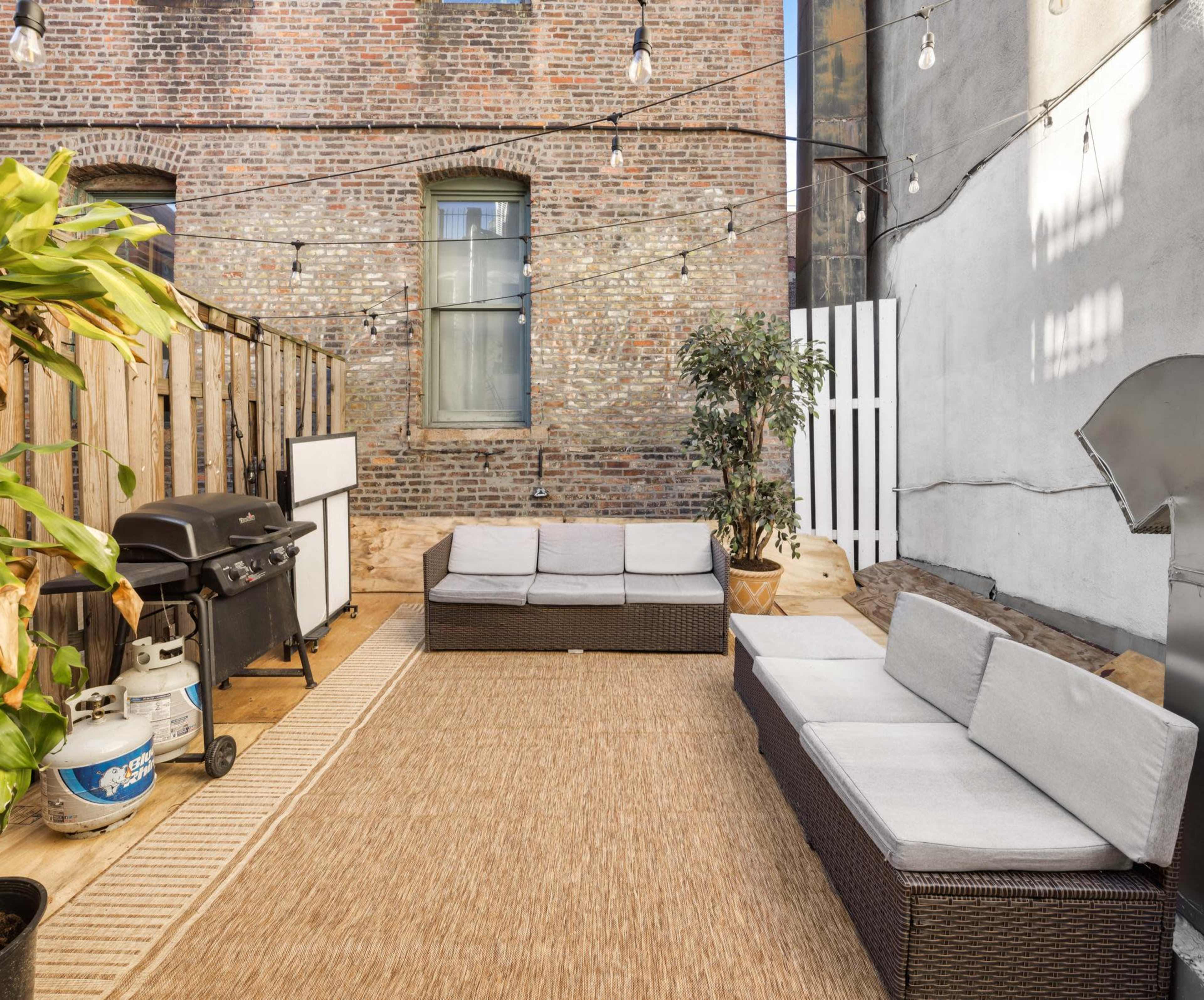 A patio area with patio furniture, a gas grill, and decorative string lights against a brick wall backdrop.