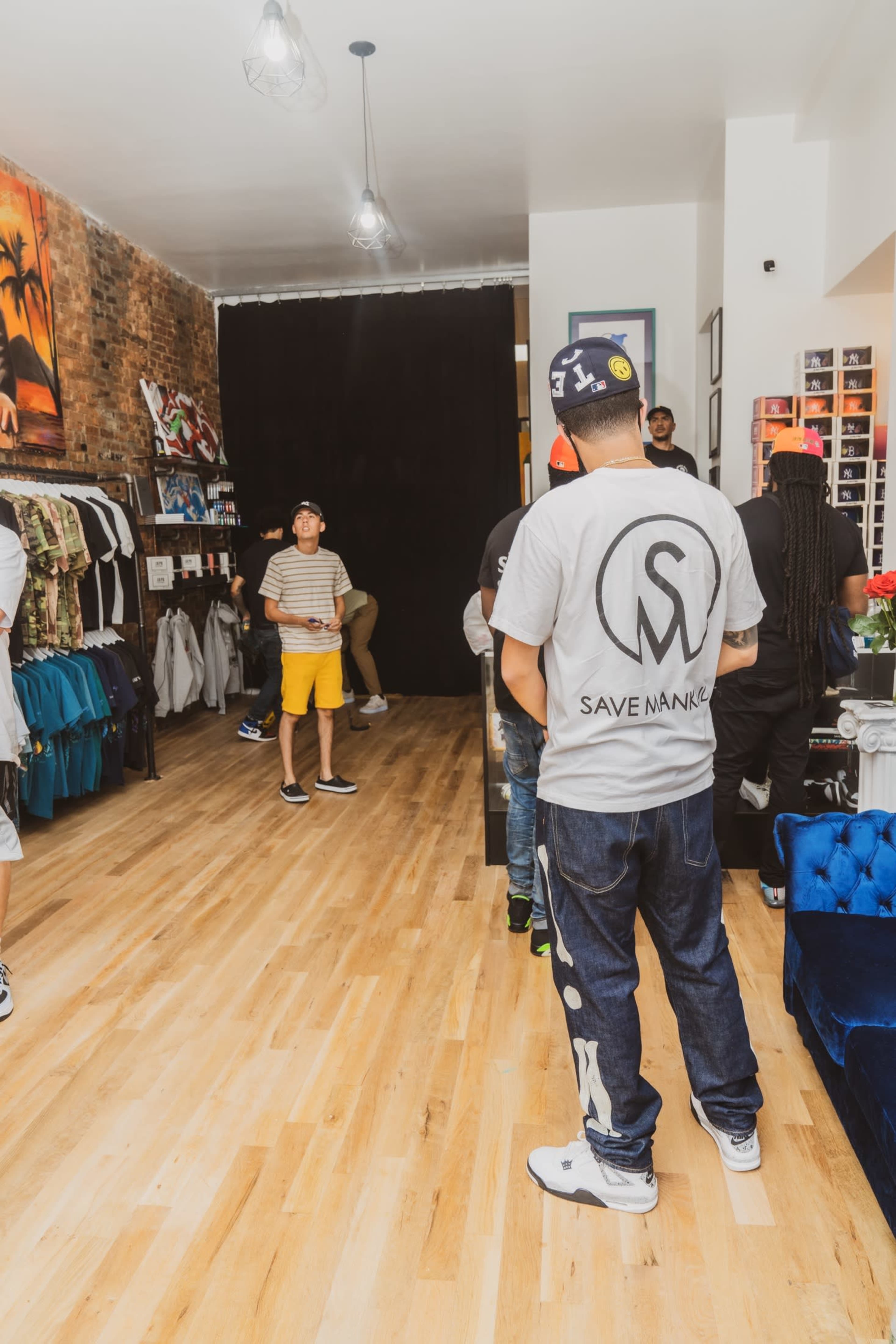 The image shows a clothing store interior with customers browsing and a black backdrop at the rear.