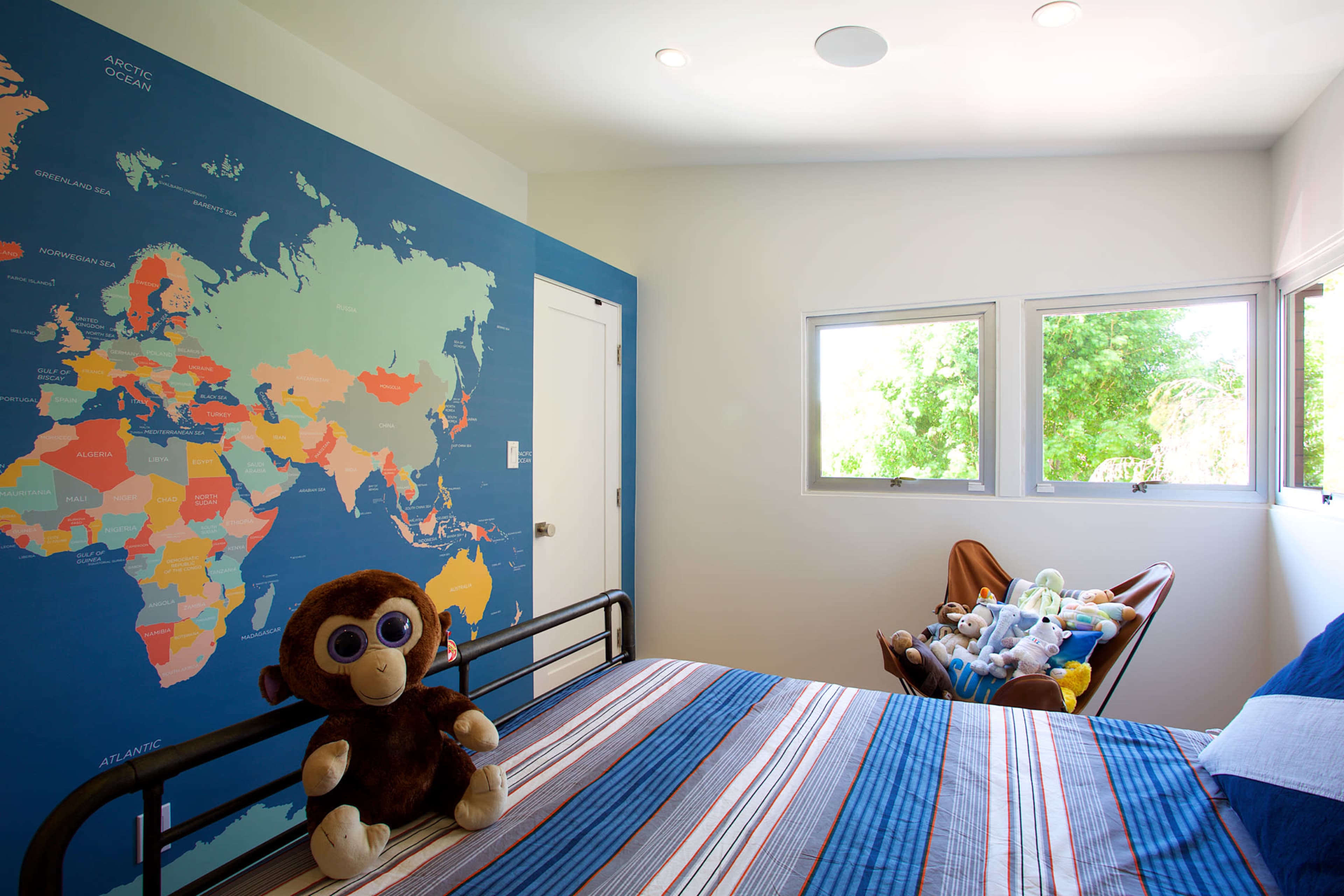 A colorful children's bedroom featuring a world map mural on one wall, a bed with striped bedding, and a cozy reading corner with stuffed animals.