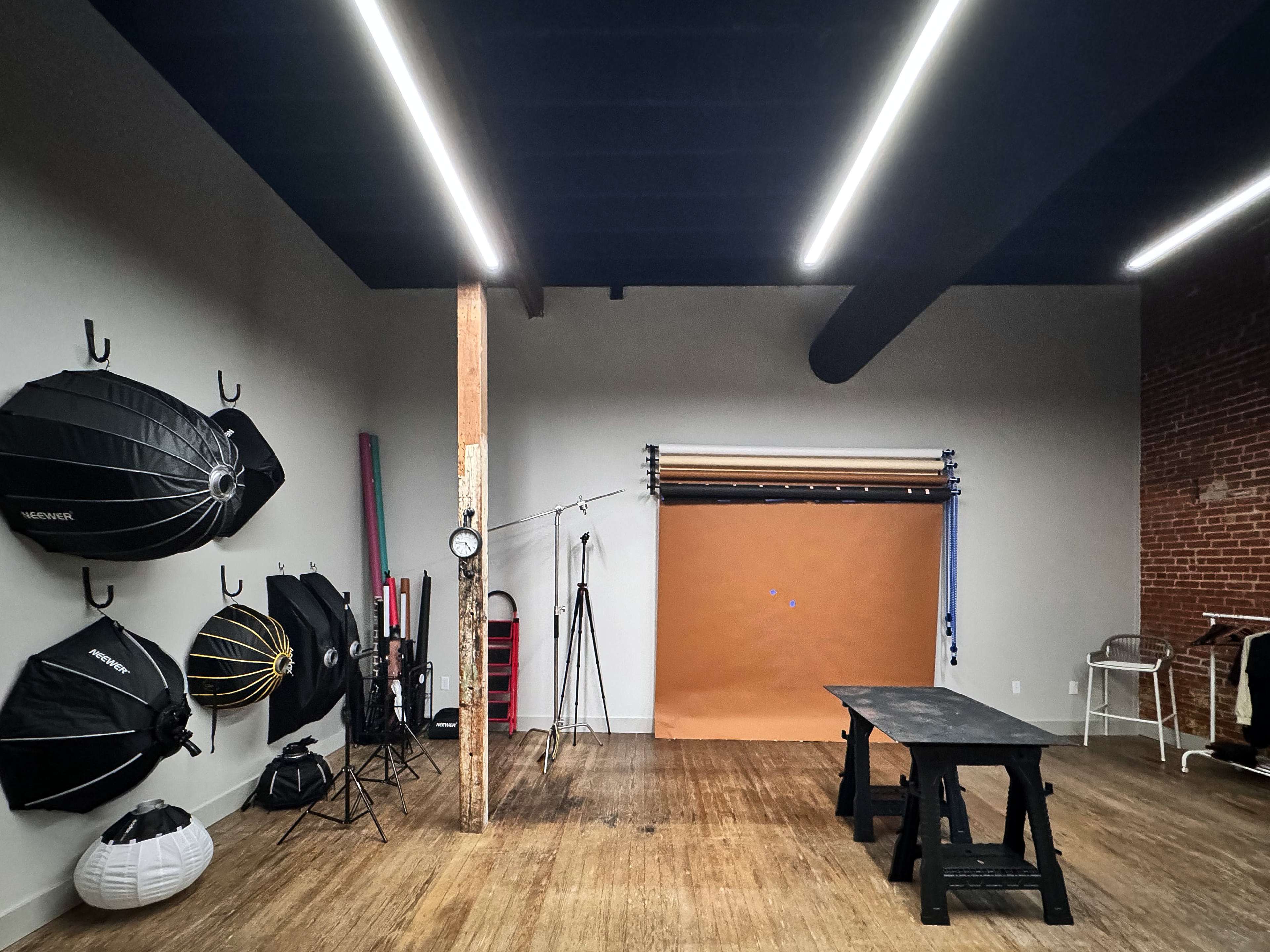 A photography studio featuring various lighting equipment, a backdrop, and wooden flooring.