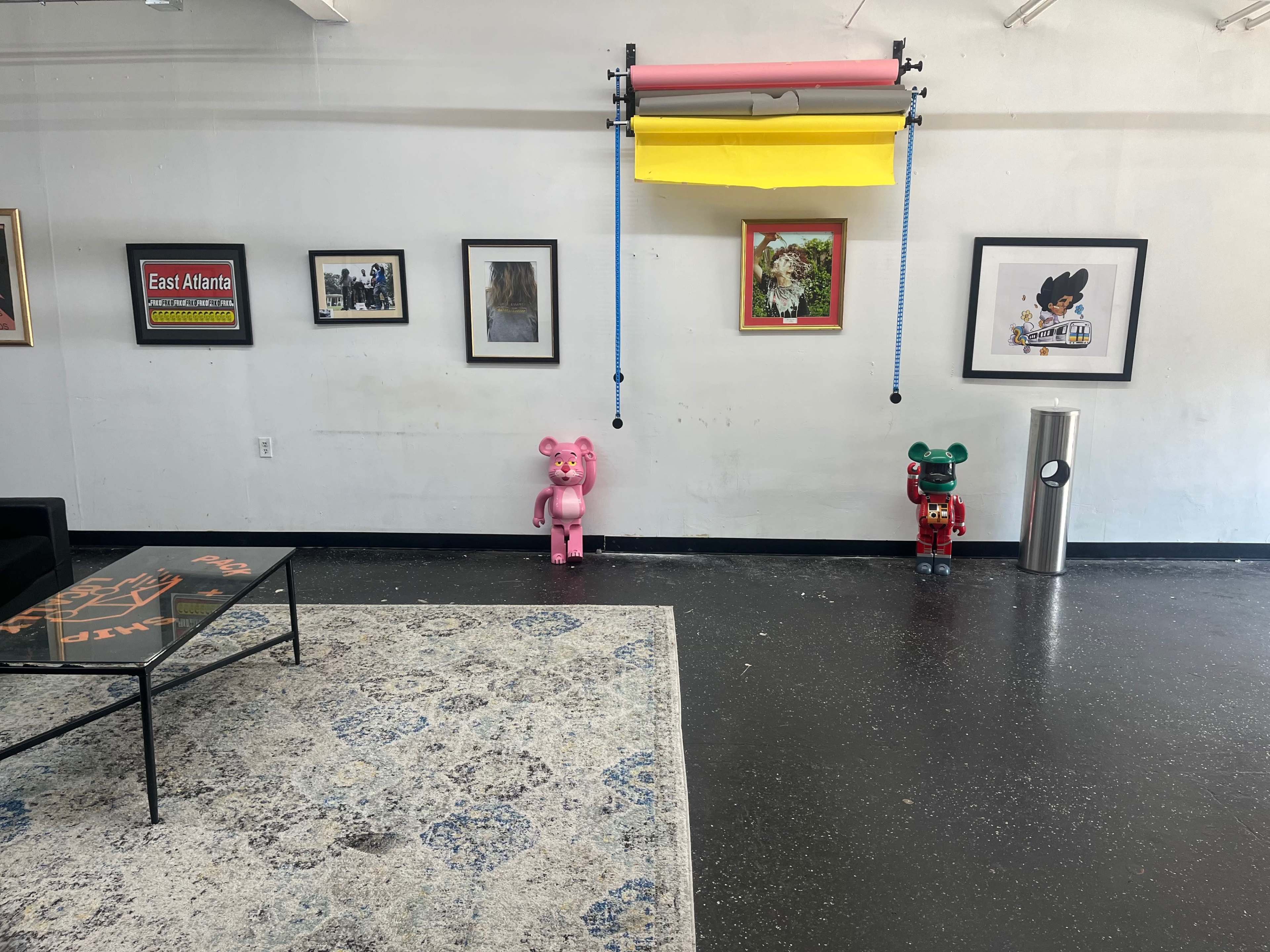 The image shows a spacious gallery with artwork on the walls, two colorful bear sculptures on the floor, and a roll of yellow and pink backdrop hanging above.