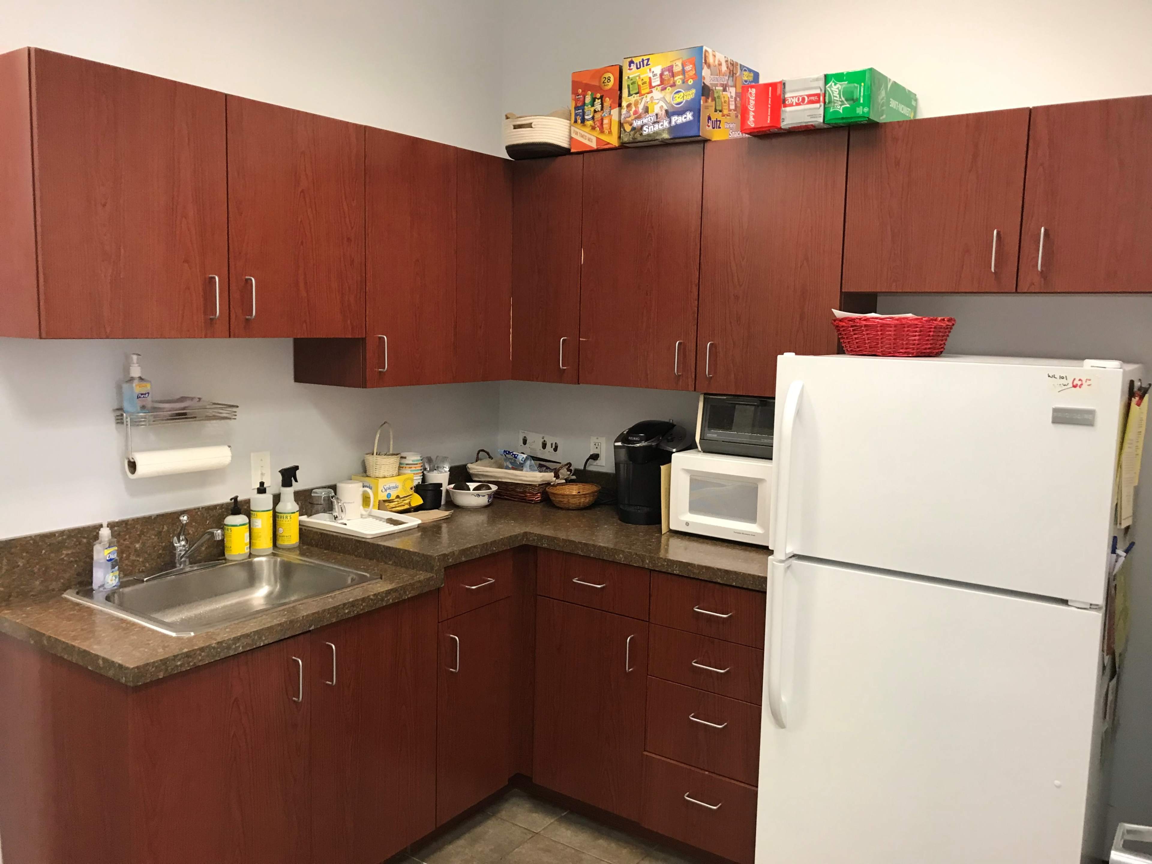 A kitchen featuring wooden cabinets, a sink, a countertop with various kitchen appliances, and a refrigerator.
