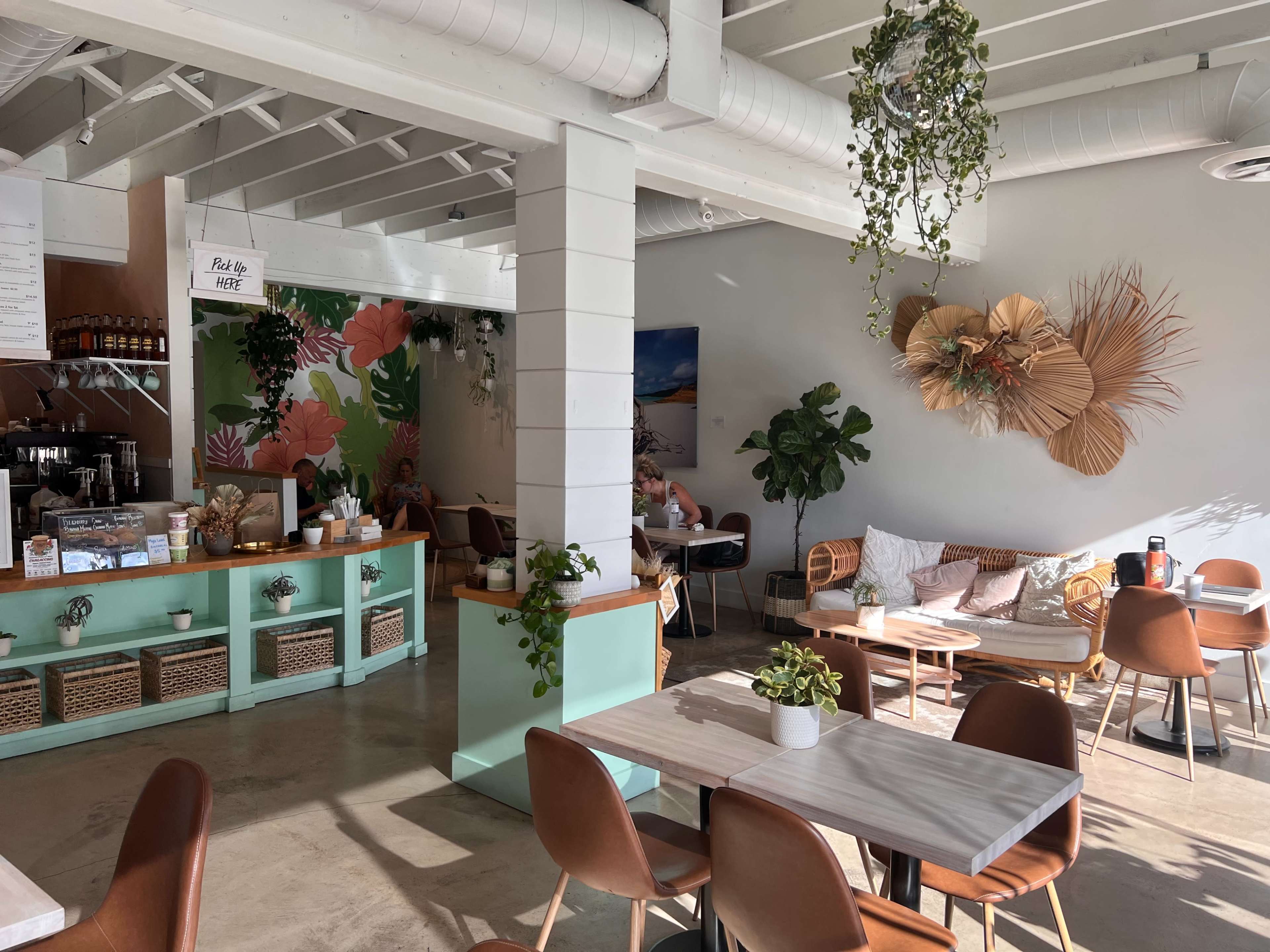 A modern café interior with green accents, wooden furniture, and various plants adorning the walls and space.