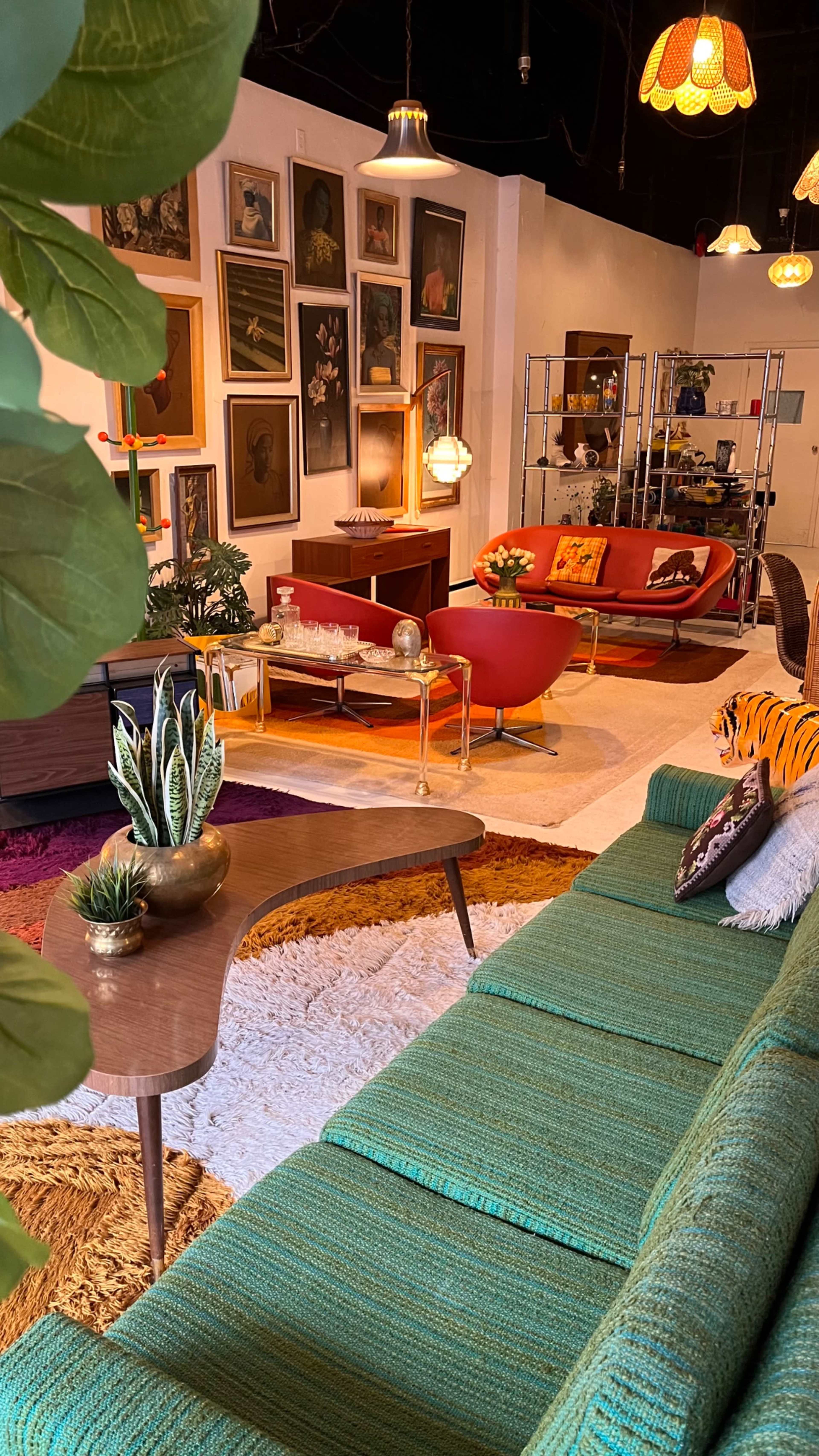 The image shows a stylish interior space featuring a green sofa, a wooden coffee table, and various pieces of decorative art on the walls.