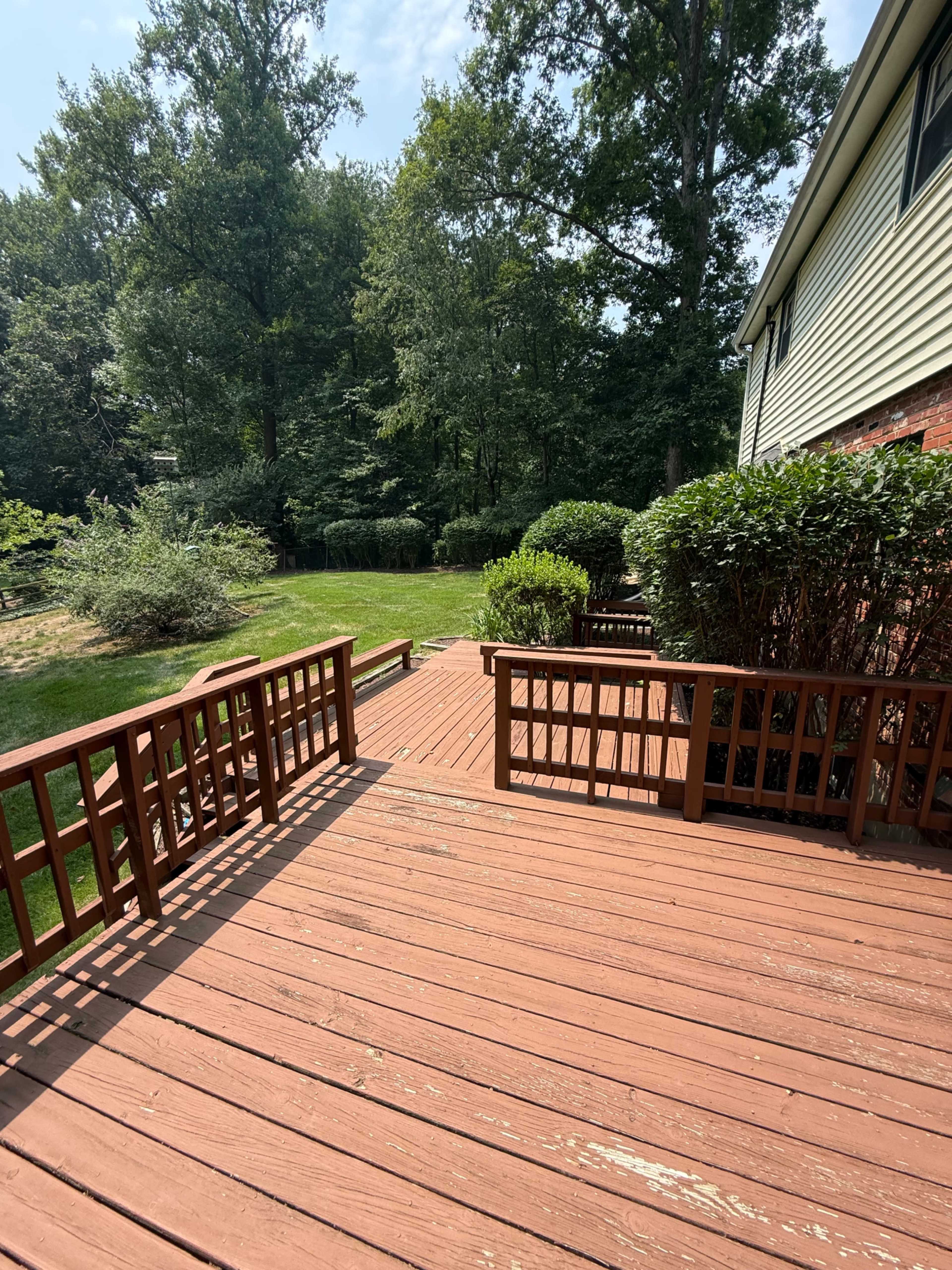 A wooden deck extends into a grassy yard surrounded by trees and bushes.