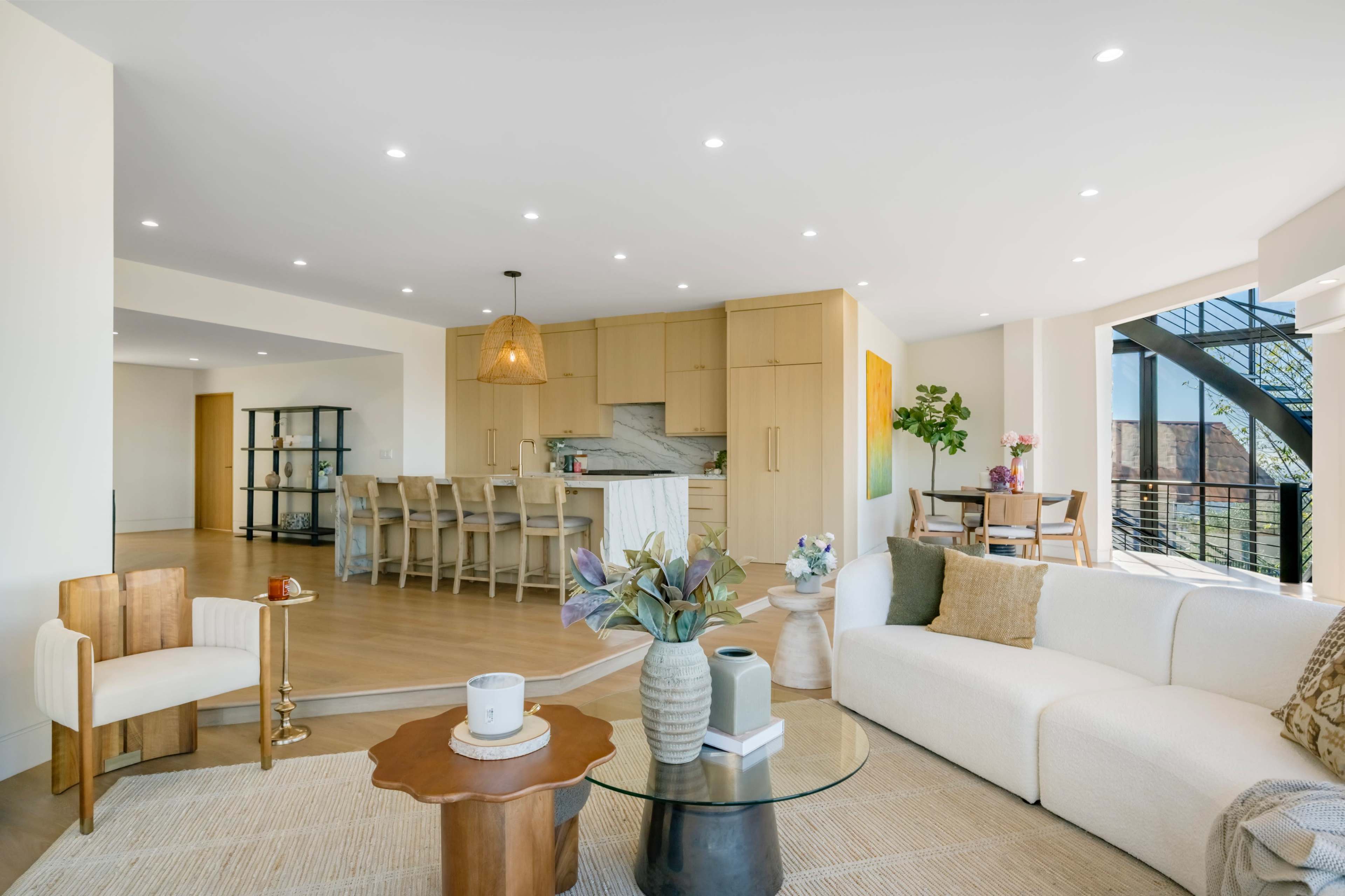 The image shows a modern living space with a white sofa, wooden furniture, a glass coffee table, and an open kitchen in the background.
