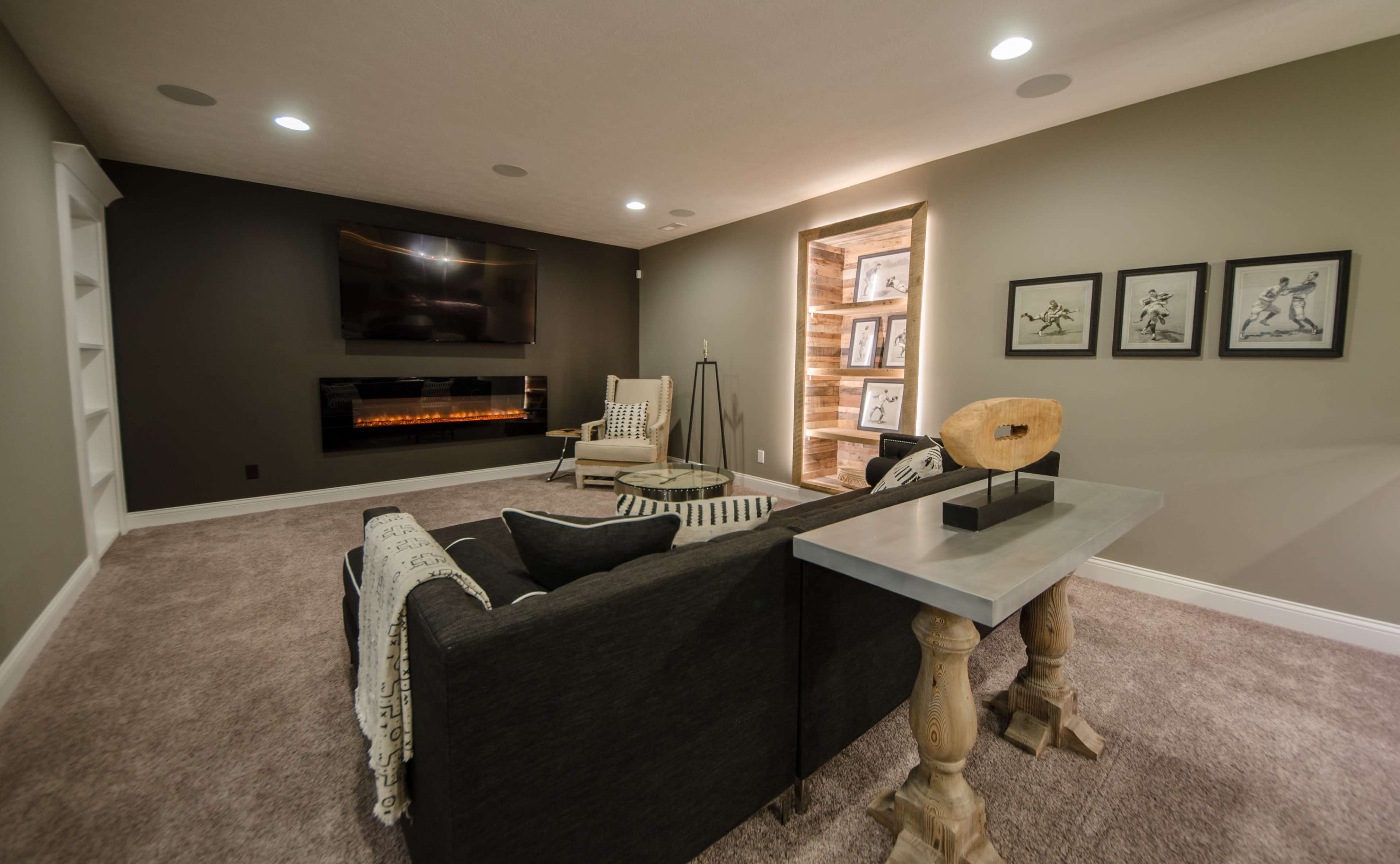 A modern living room with a dark gray wall, a wall-mounted television, an electric fireplace, and a seating area featuring a couch and a small table.