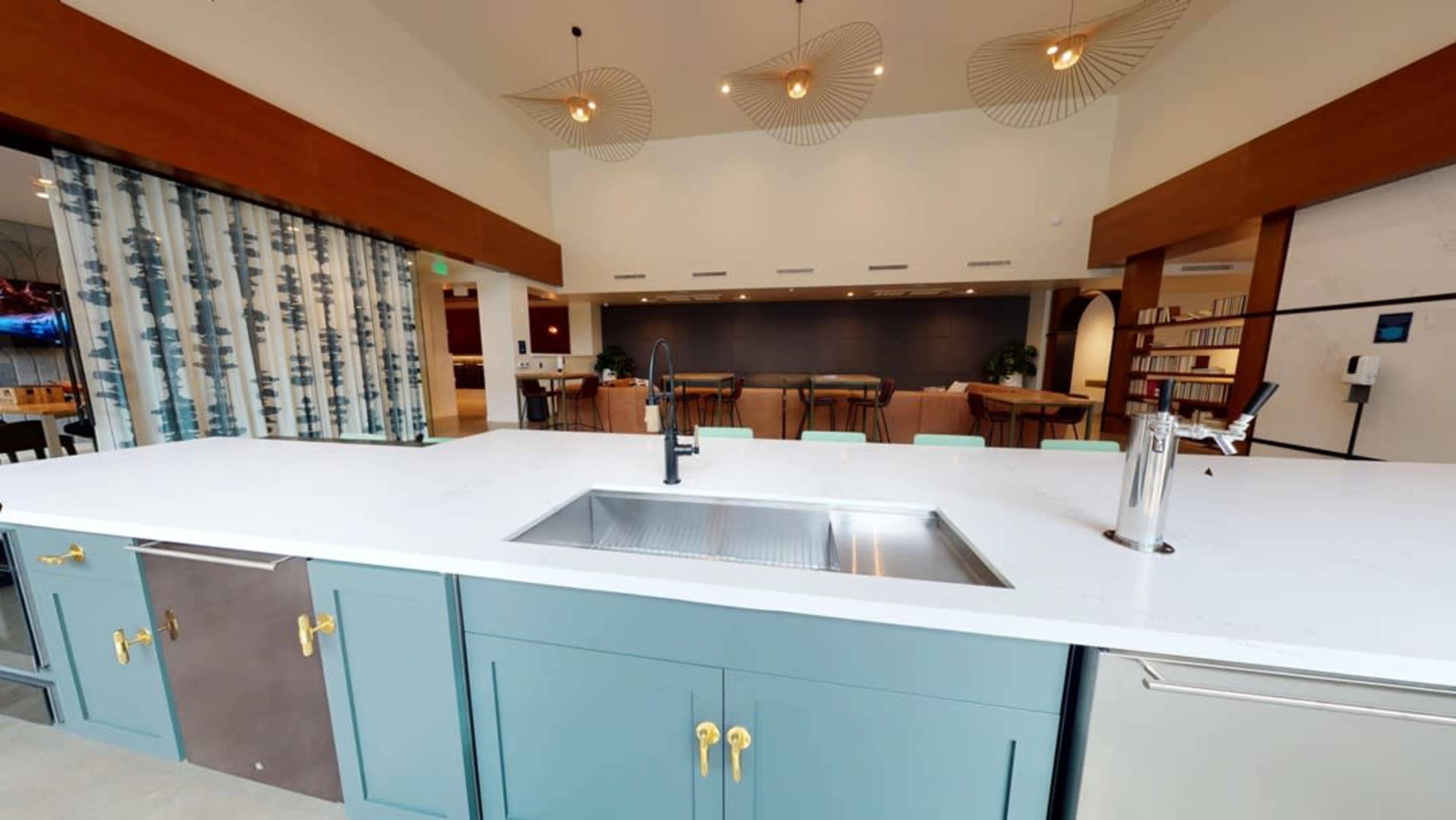A modern kitchen featuring a large island with a stainless steel sink and cabinetry in soft blue and gray tones, illuminated by pendant lights.