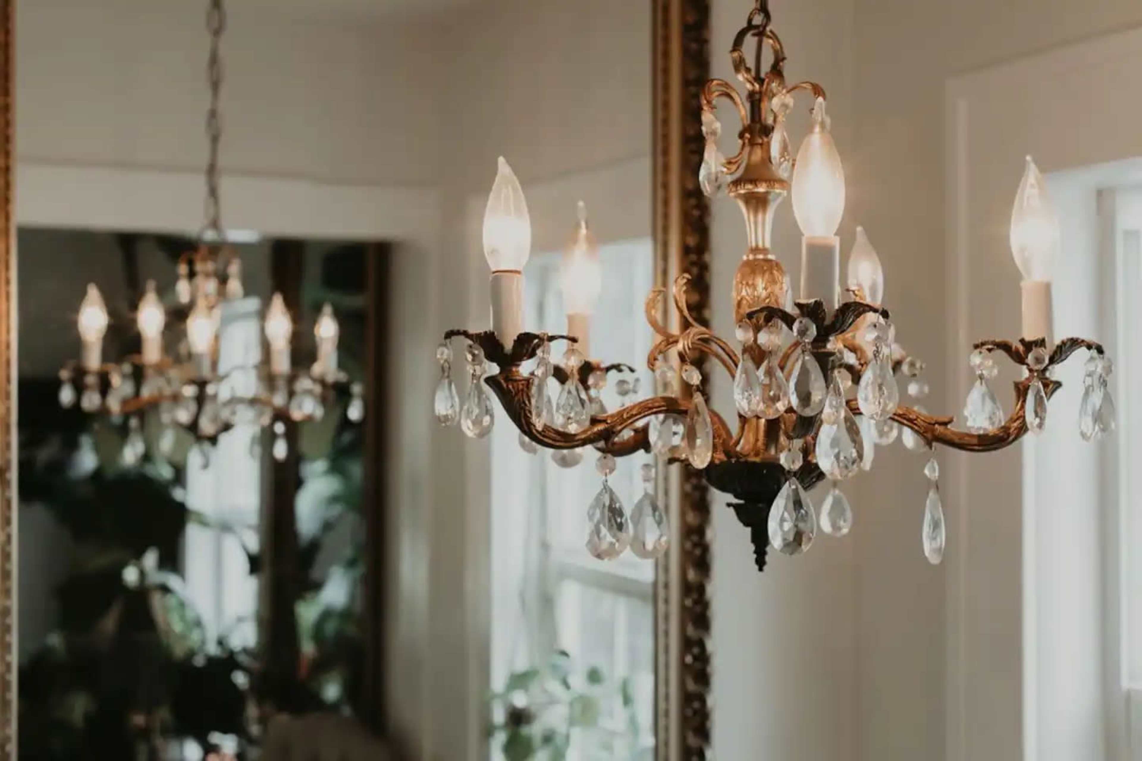 Two ornate chandeliers hanging in a room, with one reflected in a large mirror.