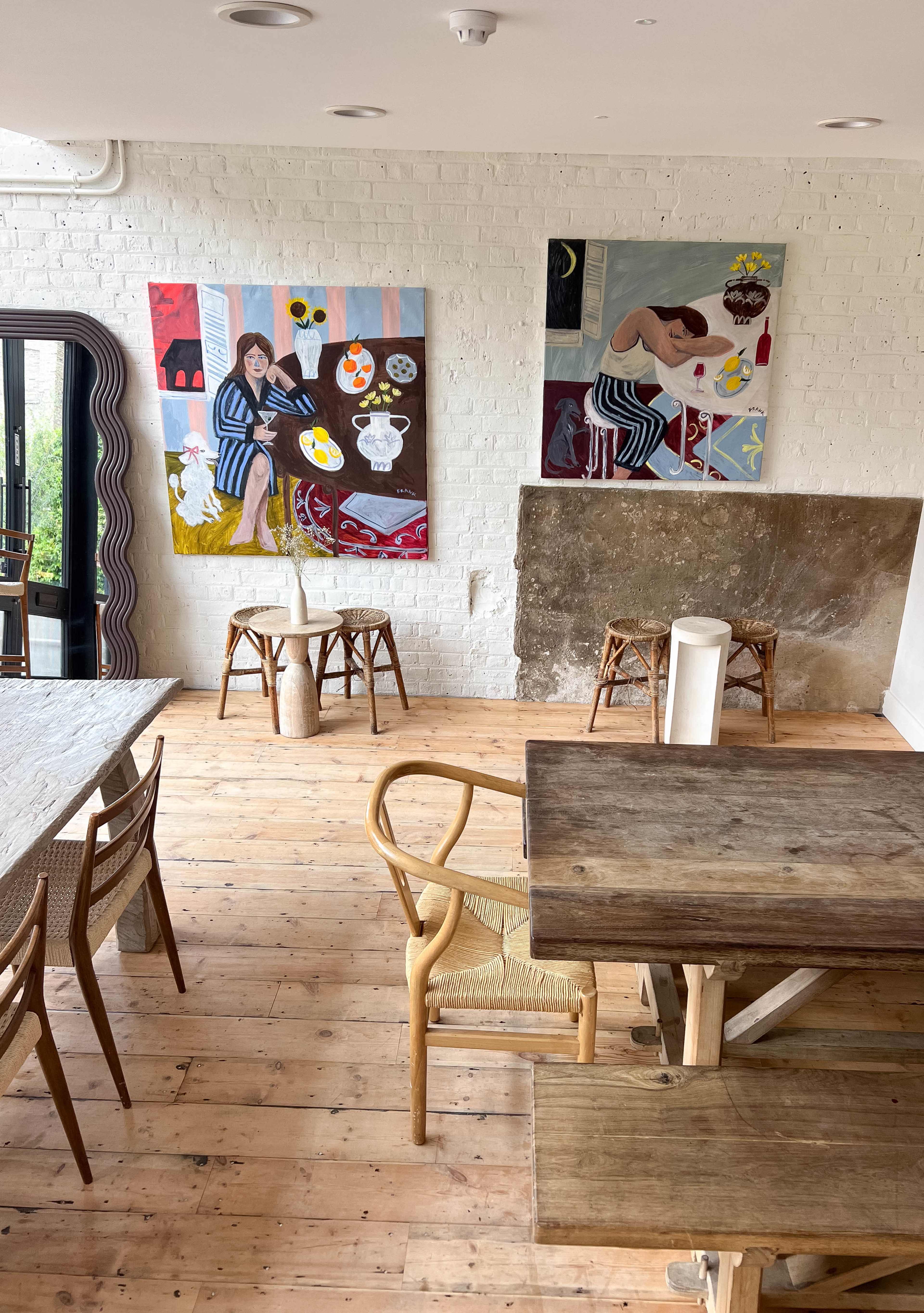 The image shows a modern café interior with wooden floors, wooden tables, and colorful artwork on the walls.