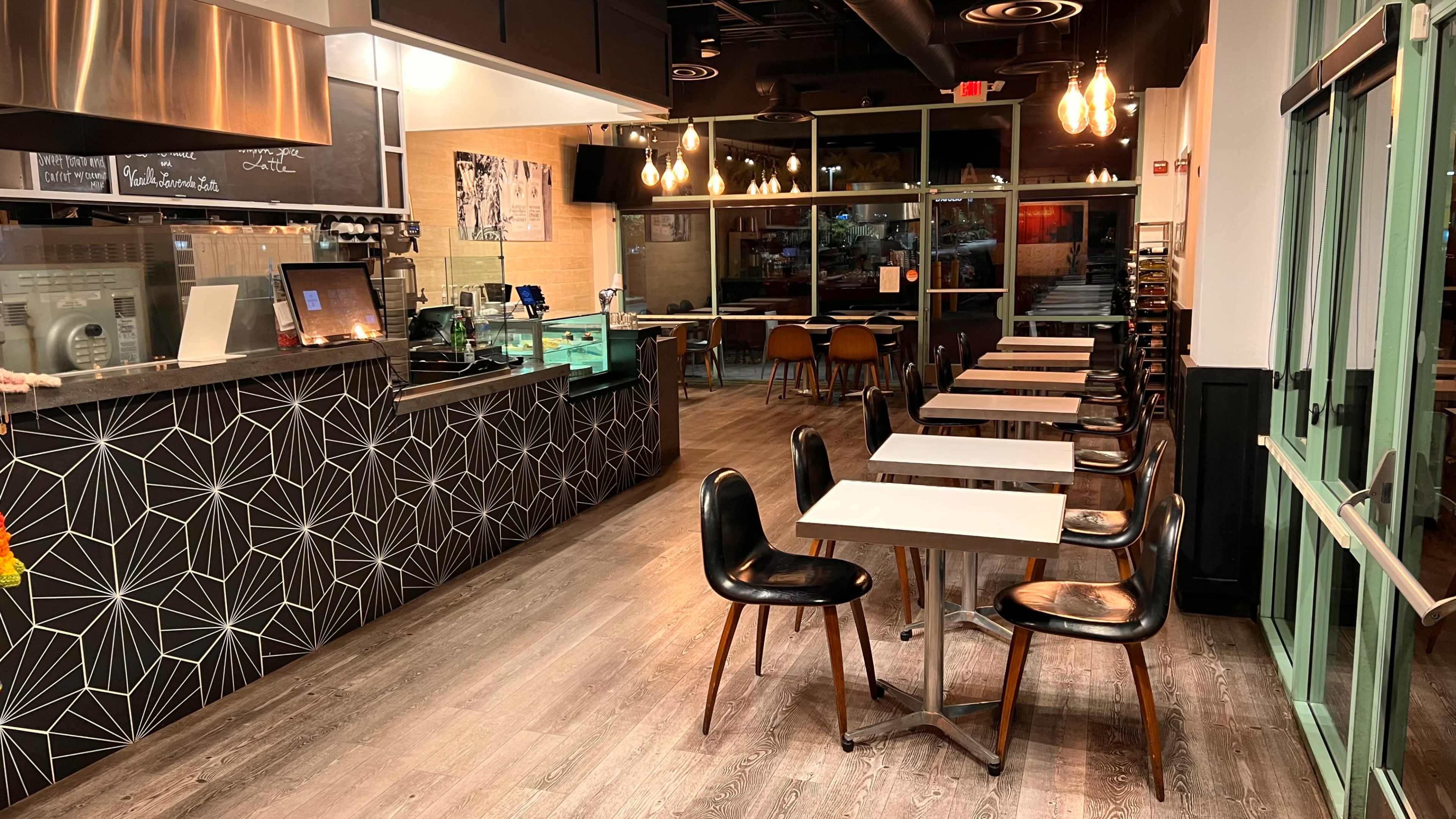 A modern café interior with a geometric patterned counter, several small tables, and a large windowed entrance.