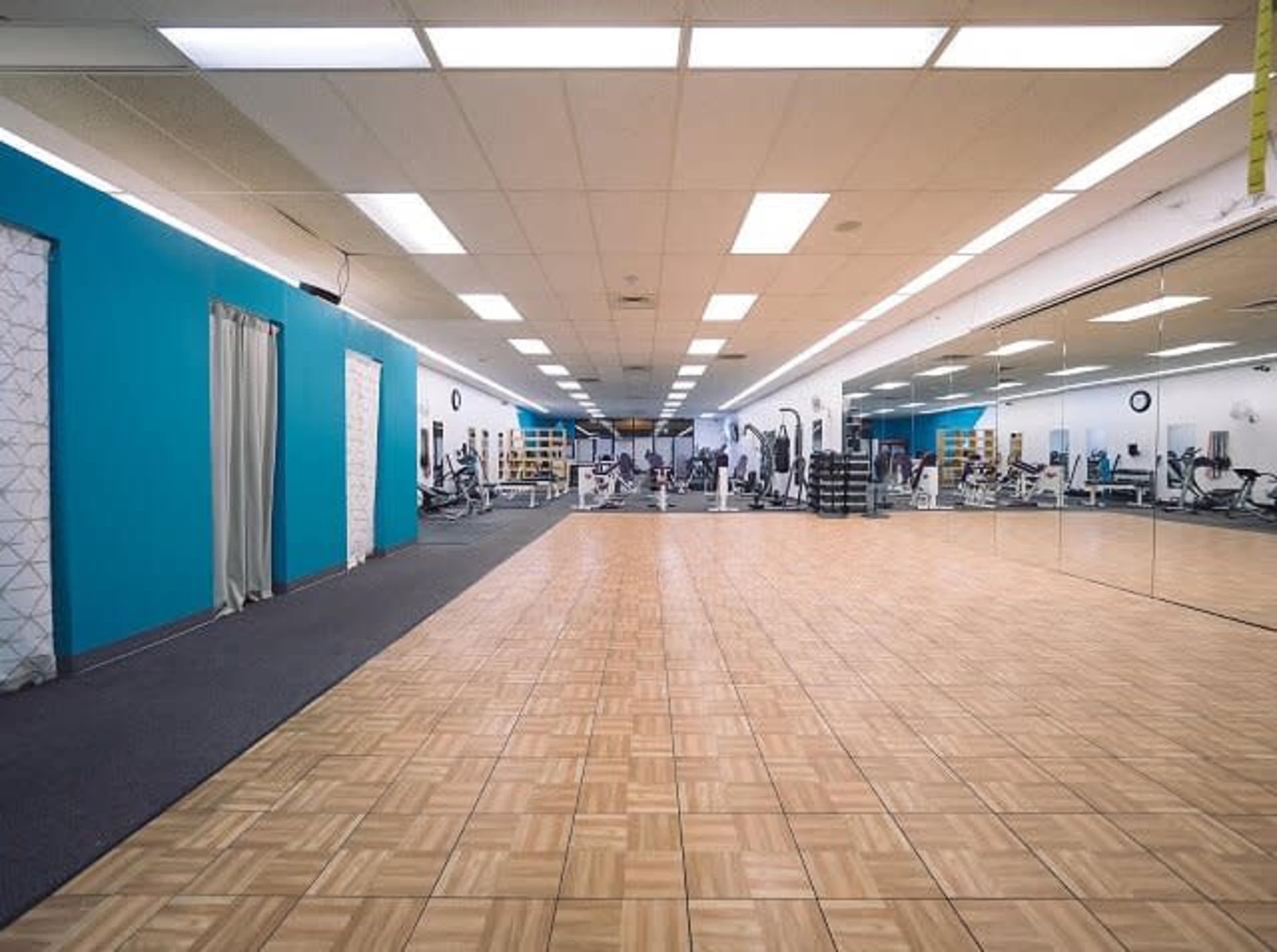 A fitness gym with exercise equipment and a mirrored wall, featuring tiled flooring and blue walls.