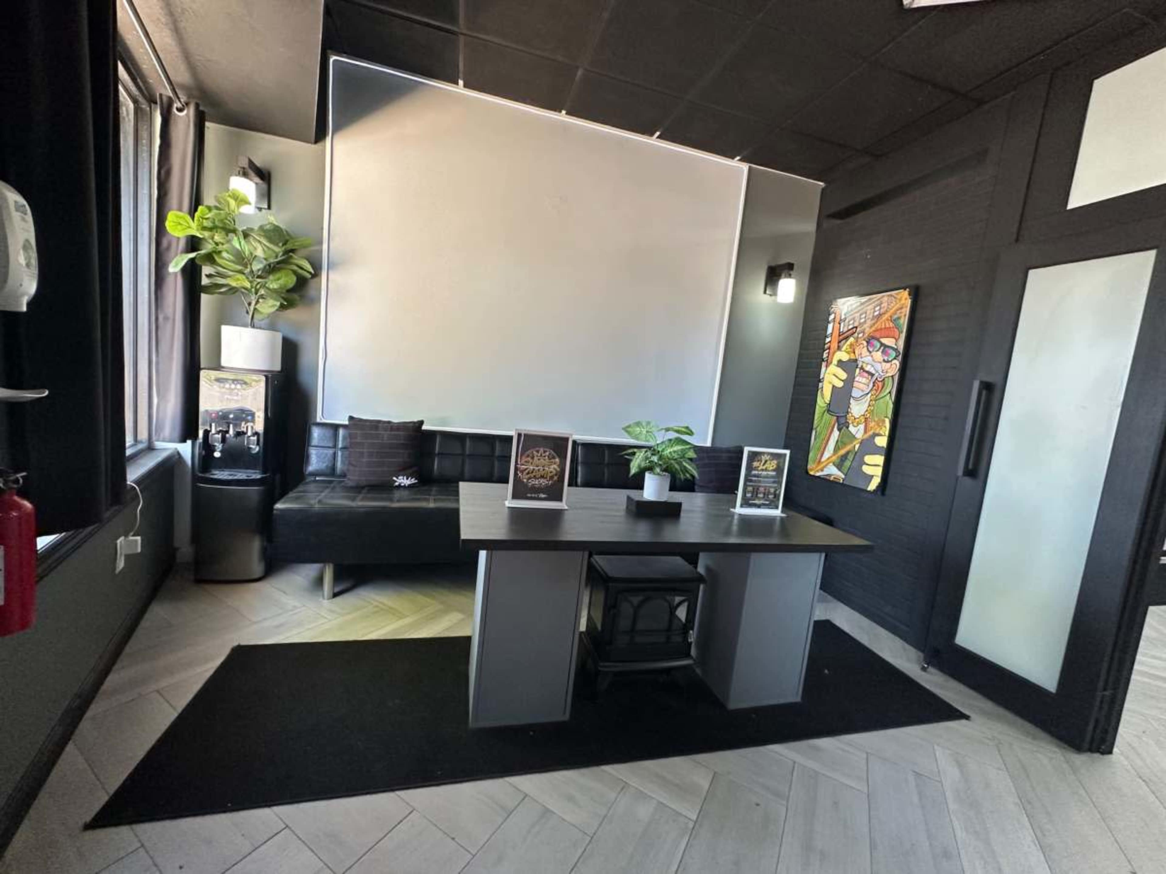 The image shows a modern reception area featuring a black couch, a table with decorative items, a plant, and a large blank wall.