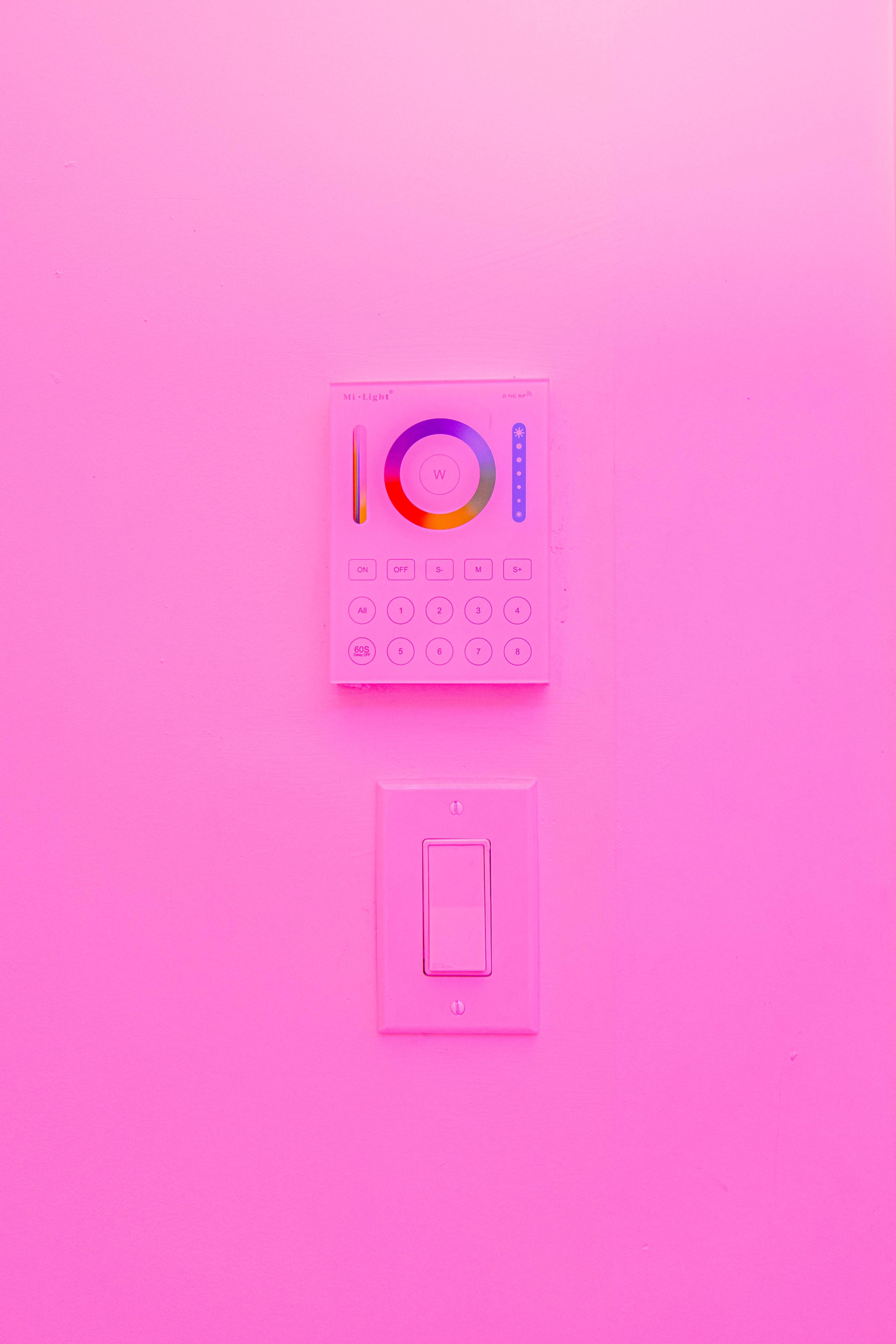 A wall-mounted control panel and light switch are displayed against a pink background.