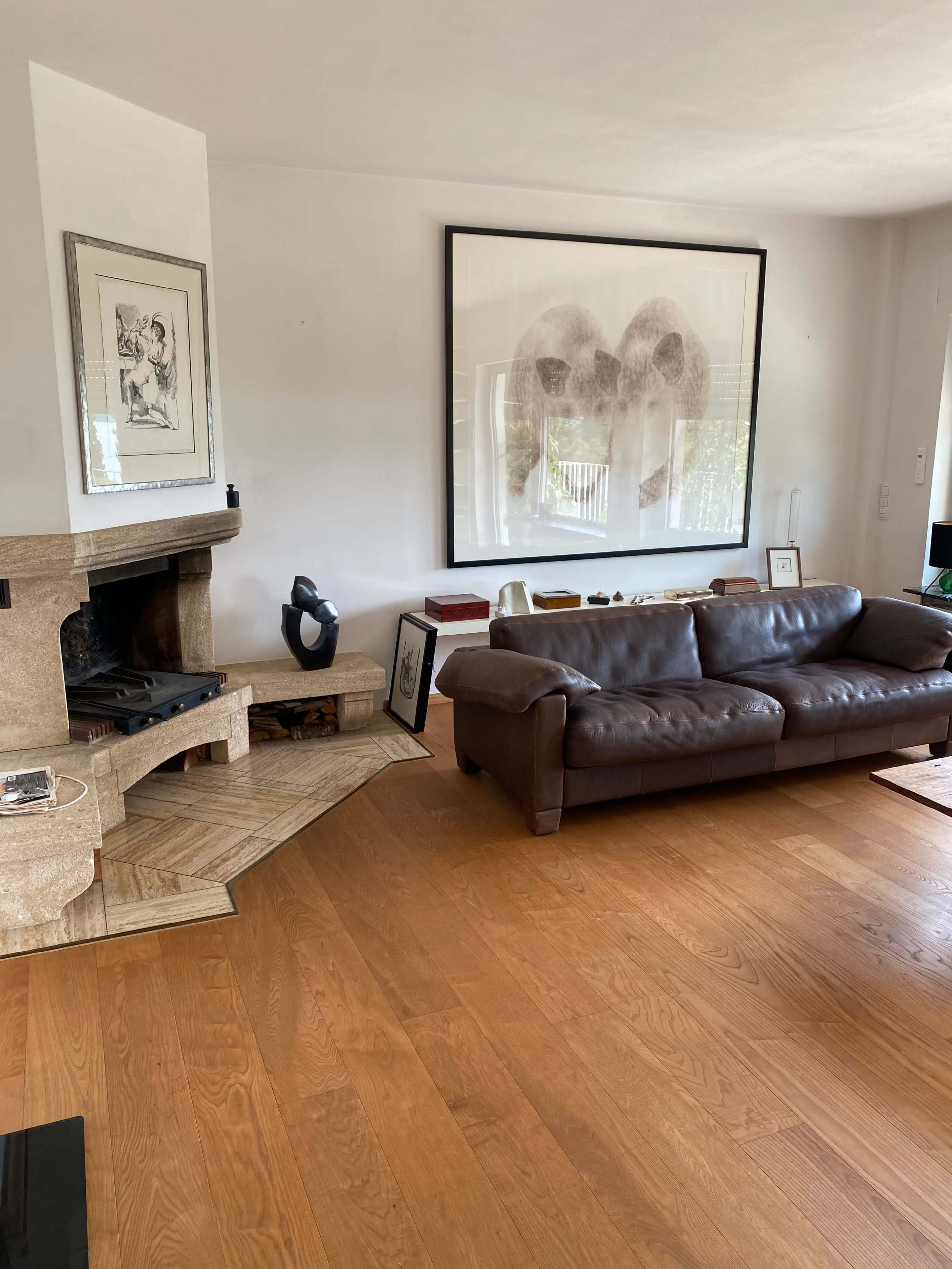 A living room with a brown leather sofa, a stone fireplace, and a large framed artwork on the wall.