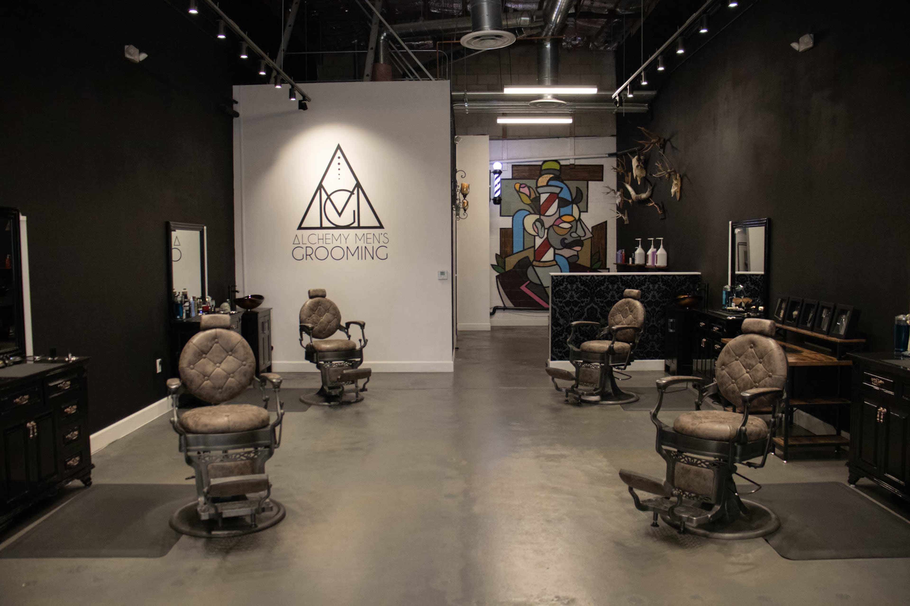 A modern barbershop with four vintage barber chairs arranged in a spacious, industrial-style interior featuring dark walls and artistic decor.