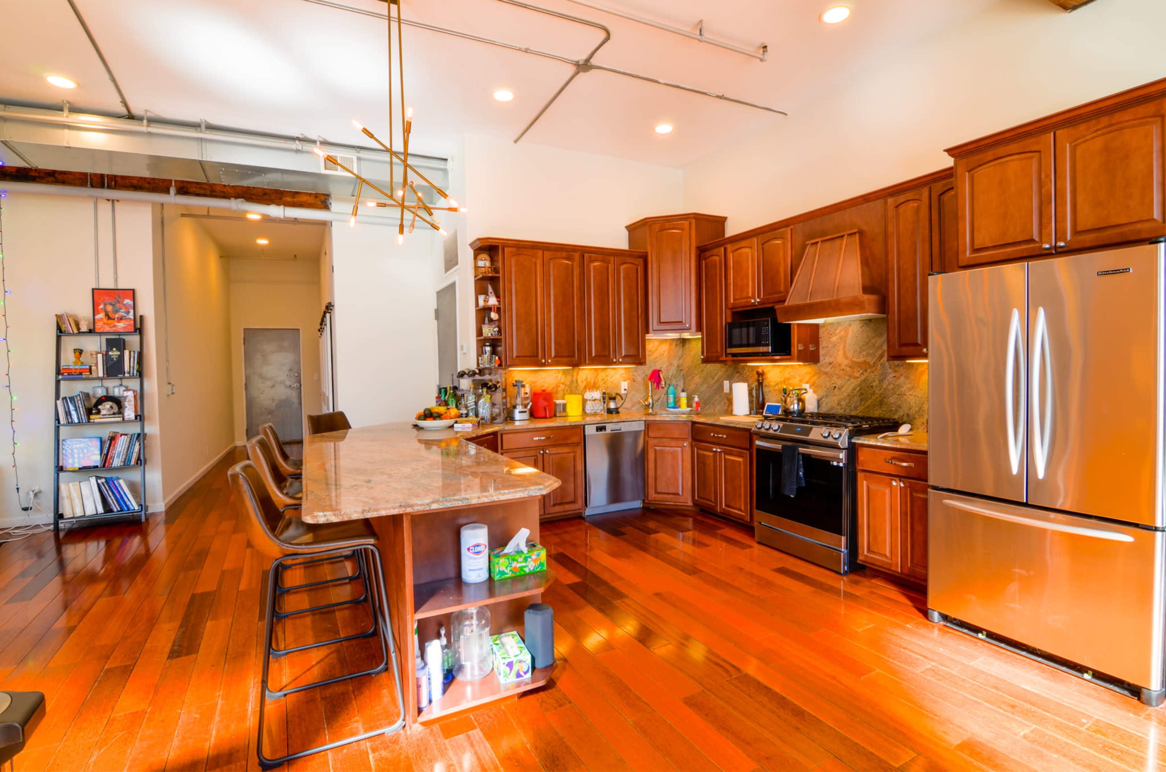 A modern kitchen with wooden cabinets, a granite countertop, stainless steel appliances, and hardwood flooring.