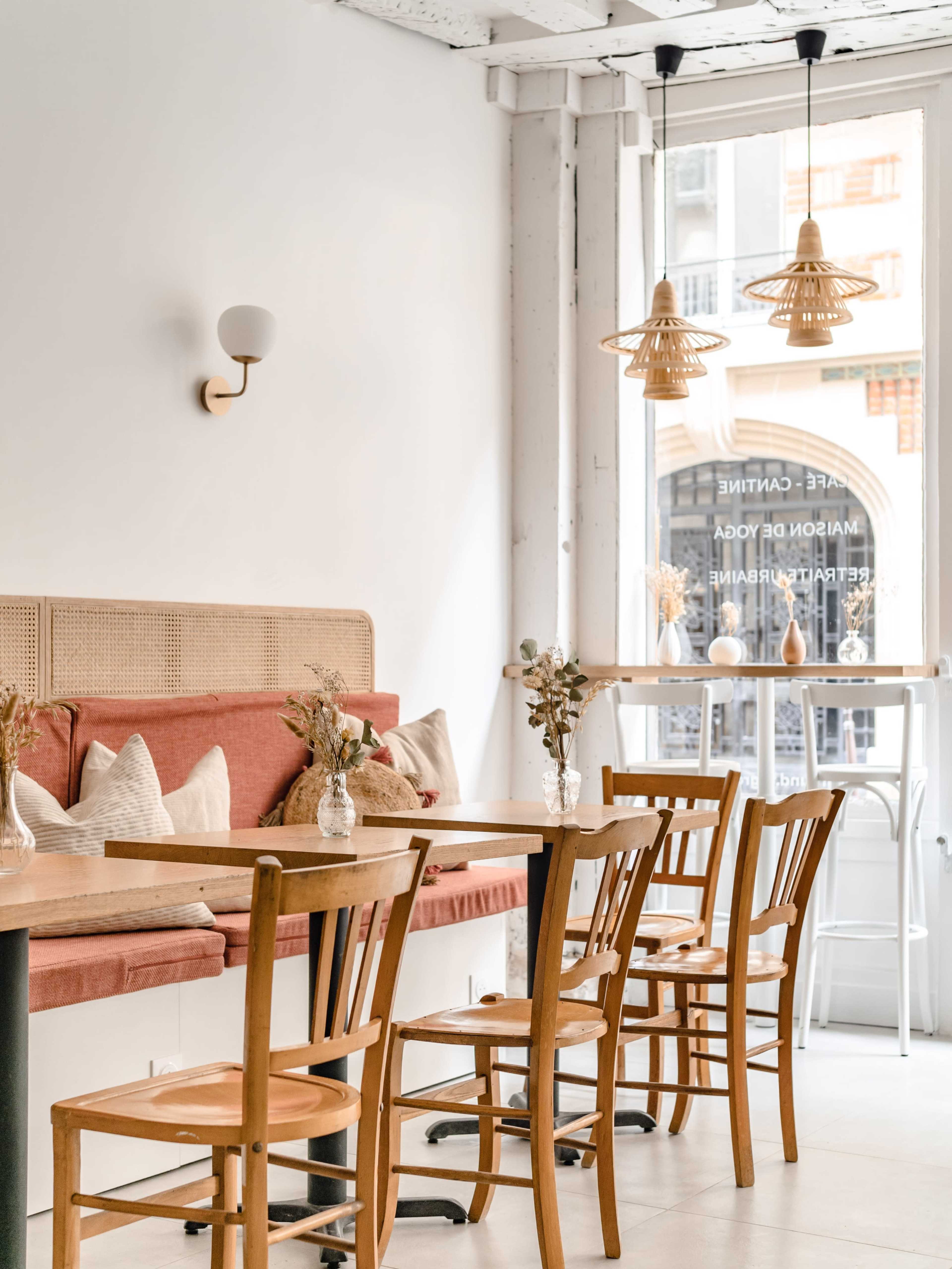 The image shows a modern café interior with wooden tables and chairs, a red upholstered bench, and pendant lighting hanging from the ceiling.