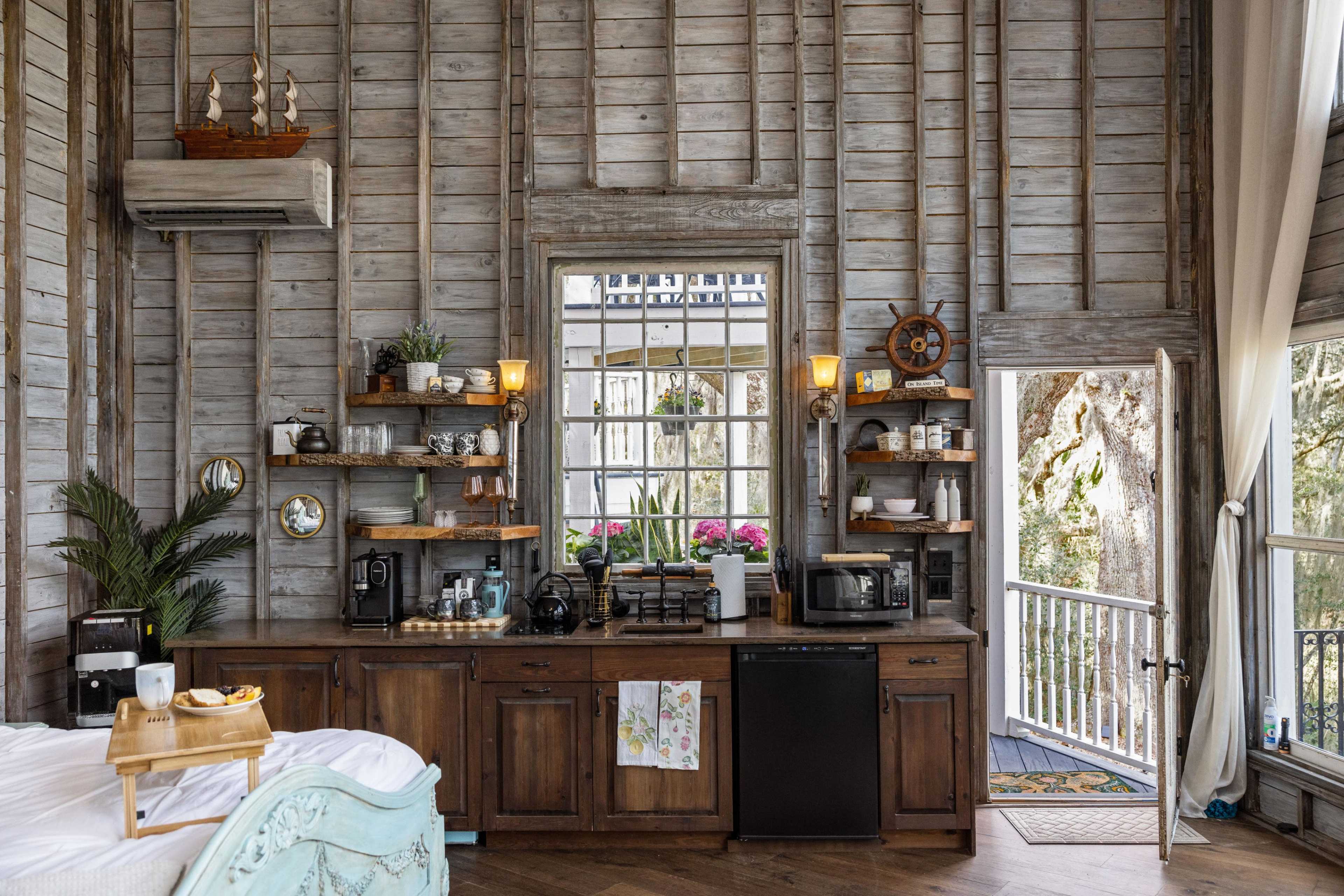 A rustic kitchen area with wooden shelves, a black refrigerator, and a large mirror, all within a cabin-style room featuring exposed wooden walls.