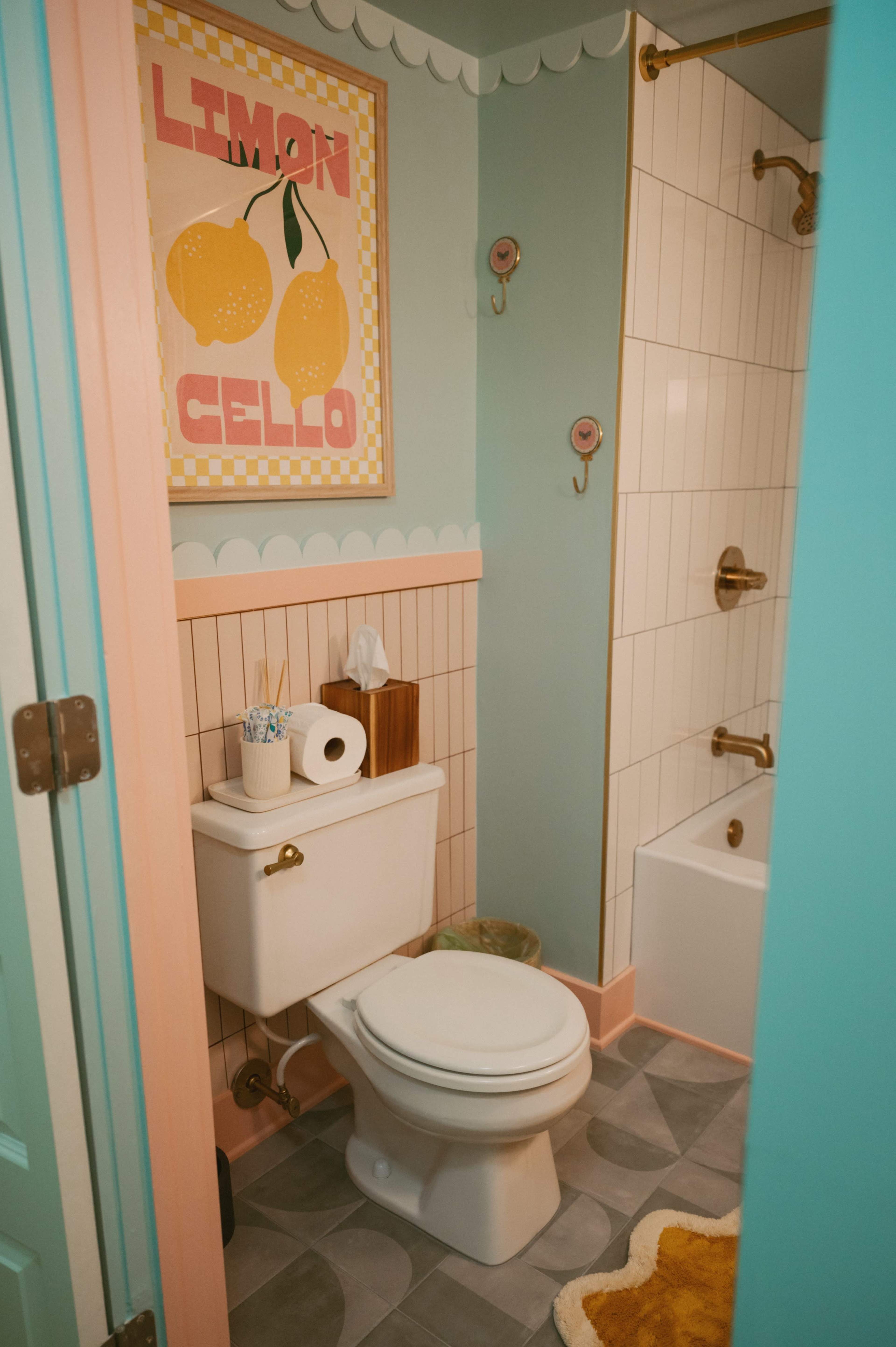 A brightly colored bathroom featuring a toilet, a bathtub with a shower, and a framed art piece depicting lemons on the wall.
