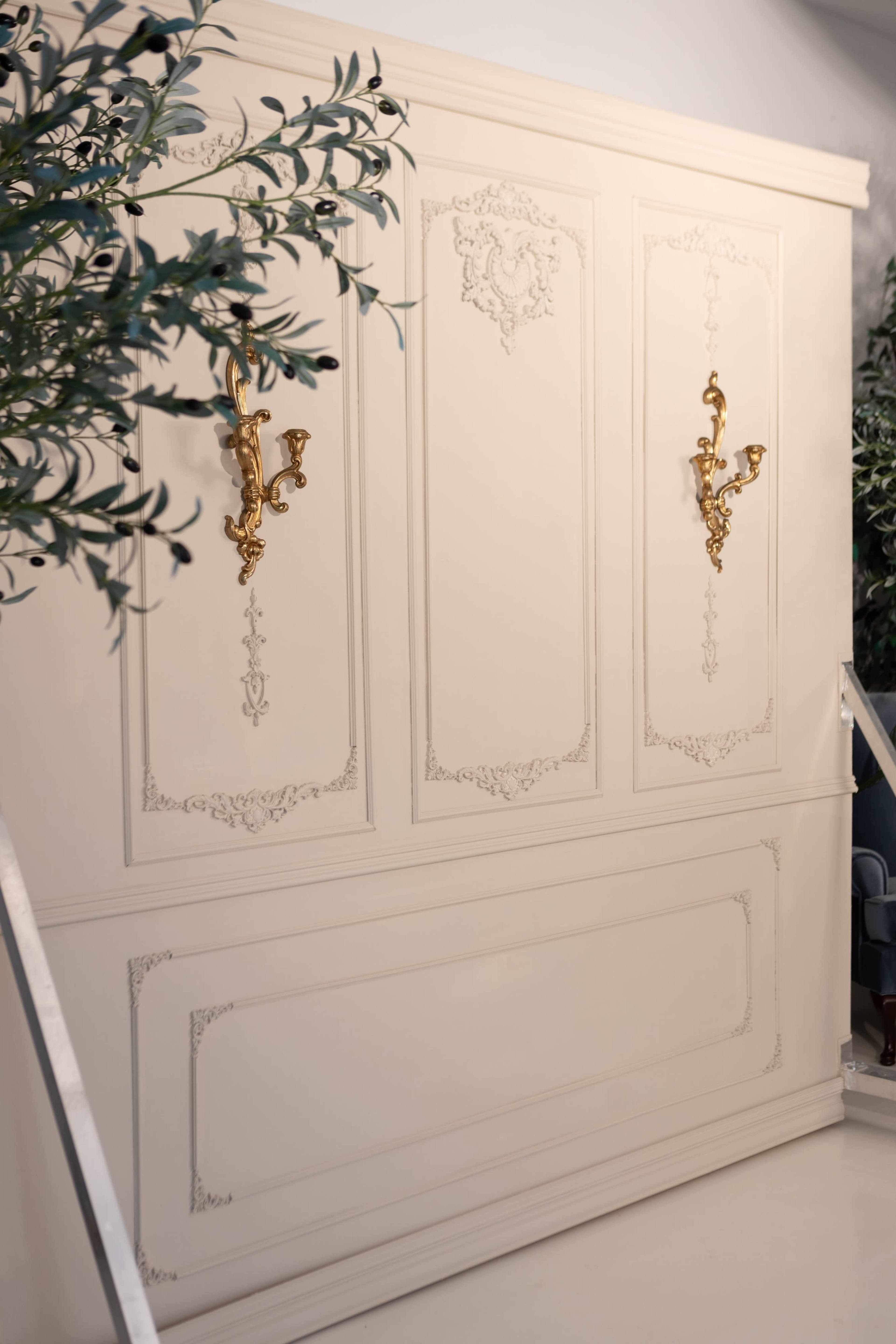 The image shows a textured white wall featuring ornate gold wall sconces and decorative paneling.