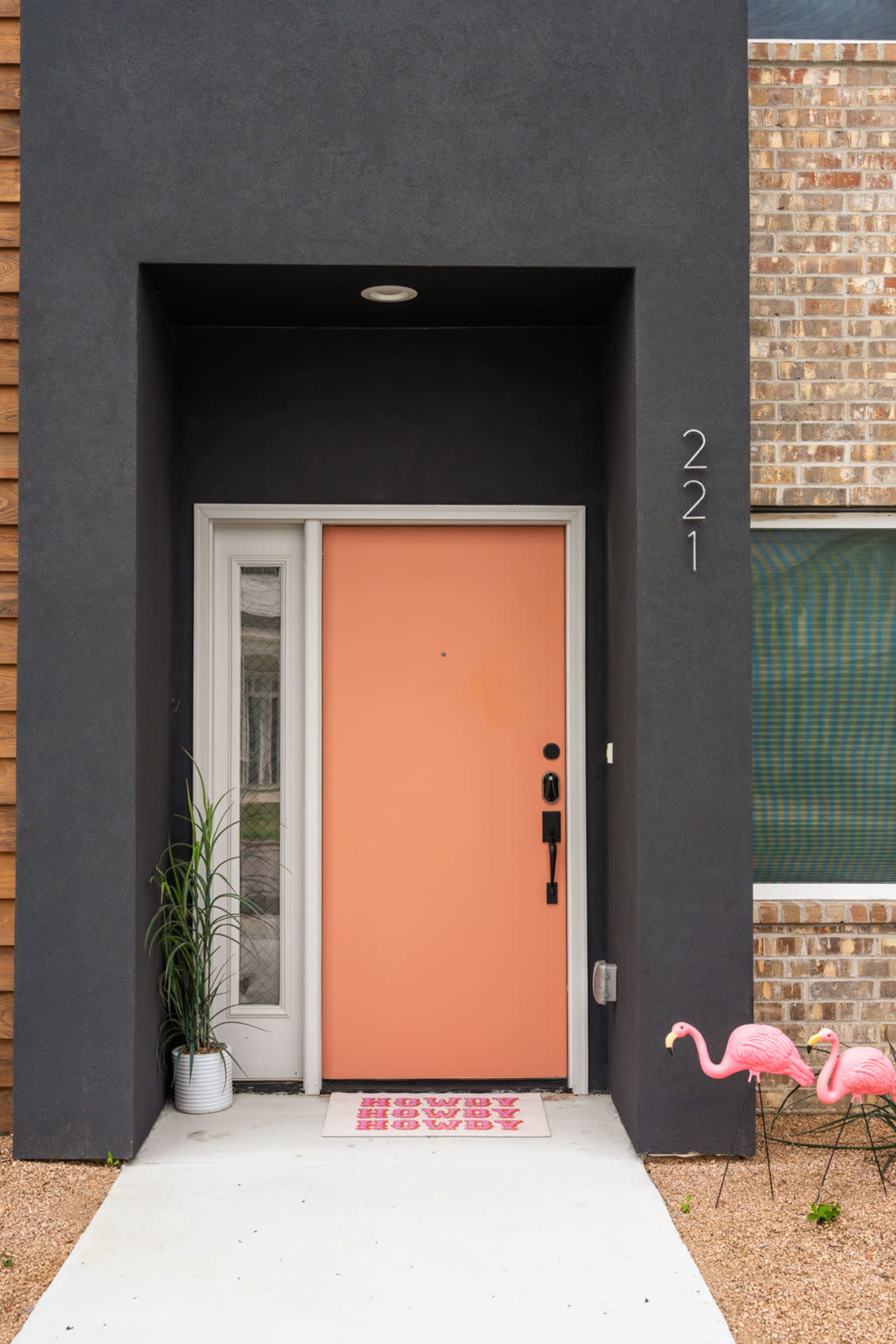 The entrance features a coral front door, flanked by a potted plant, with a welcome mat and two pink flamingo decorations outside.