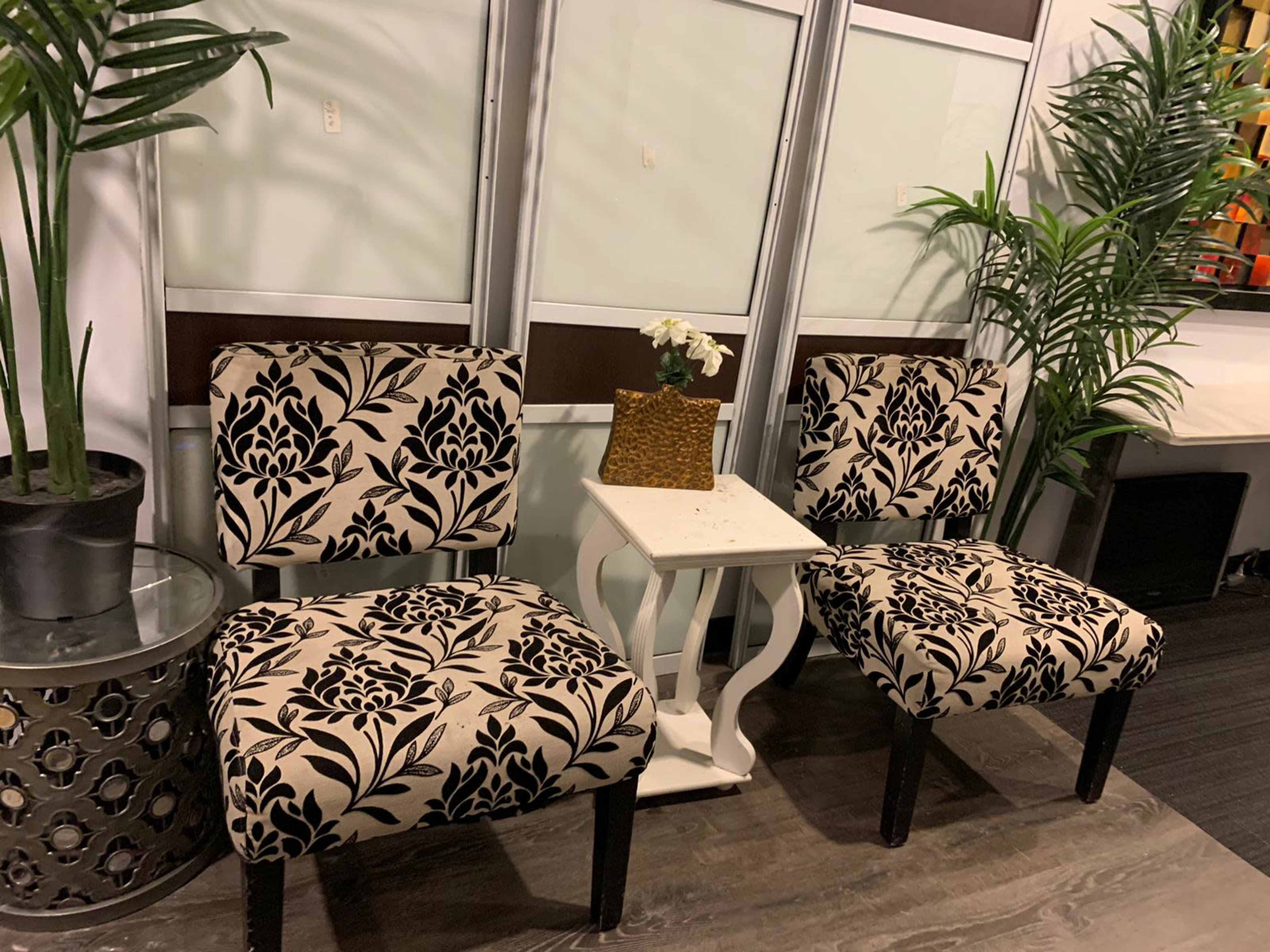 Two patterned chairs are positioned beside a small white side table topped with a decorative planter in a neatly arranged indoor space.