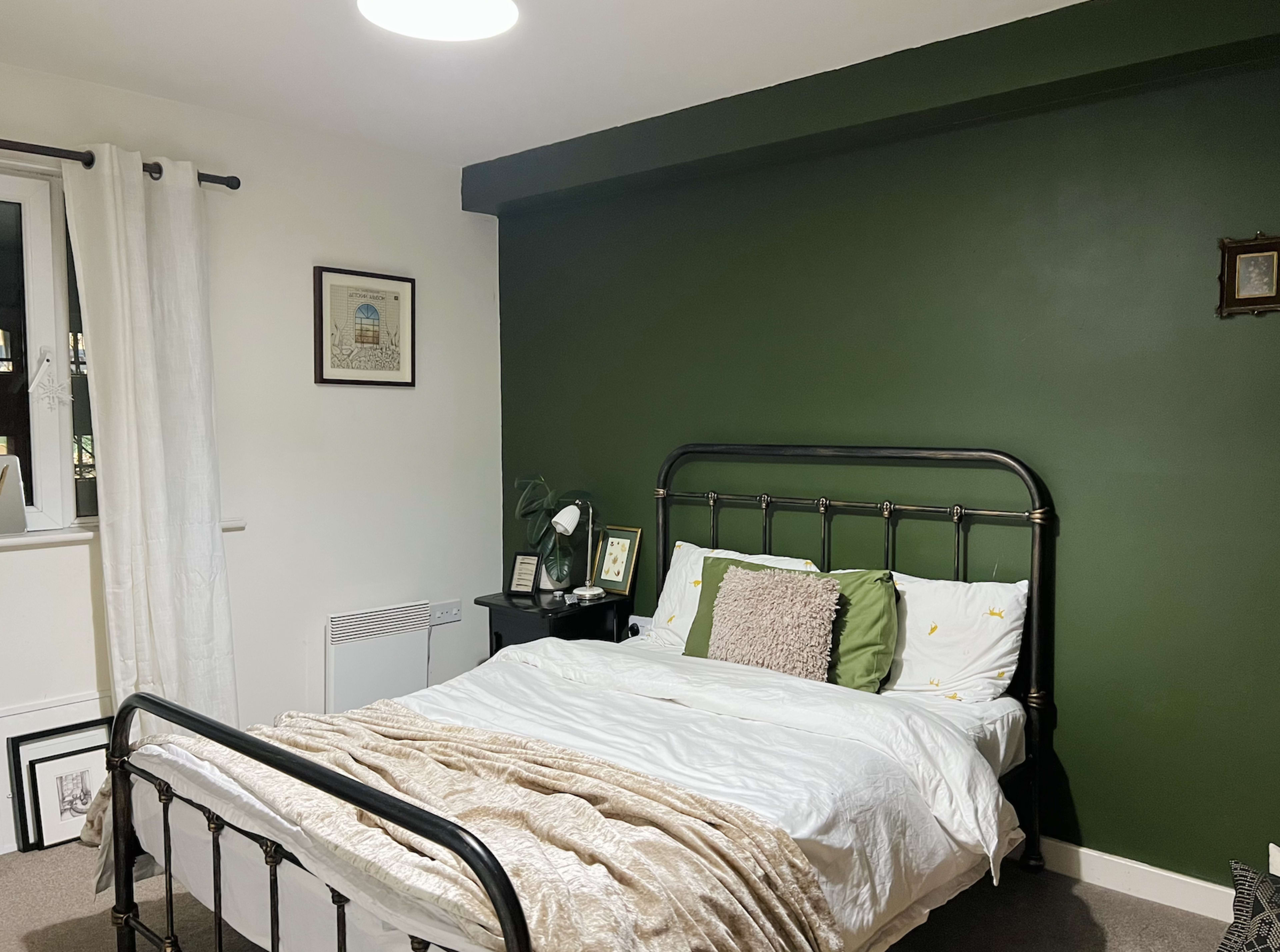 A bedroom with a black metal bed frame, green wall, white bedding, and a small nightstand beside it.