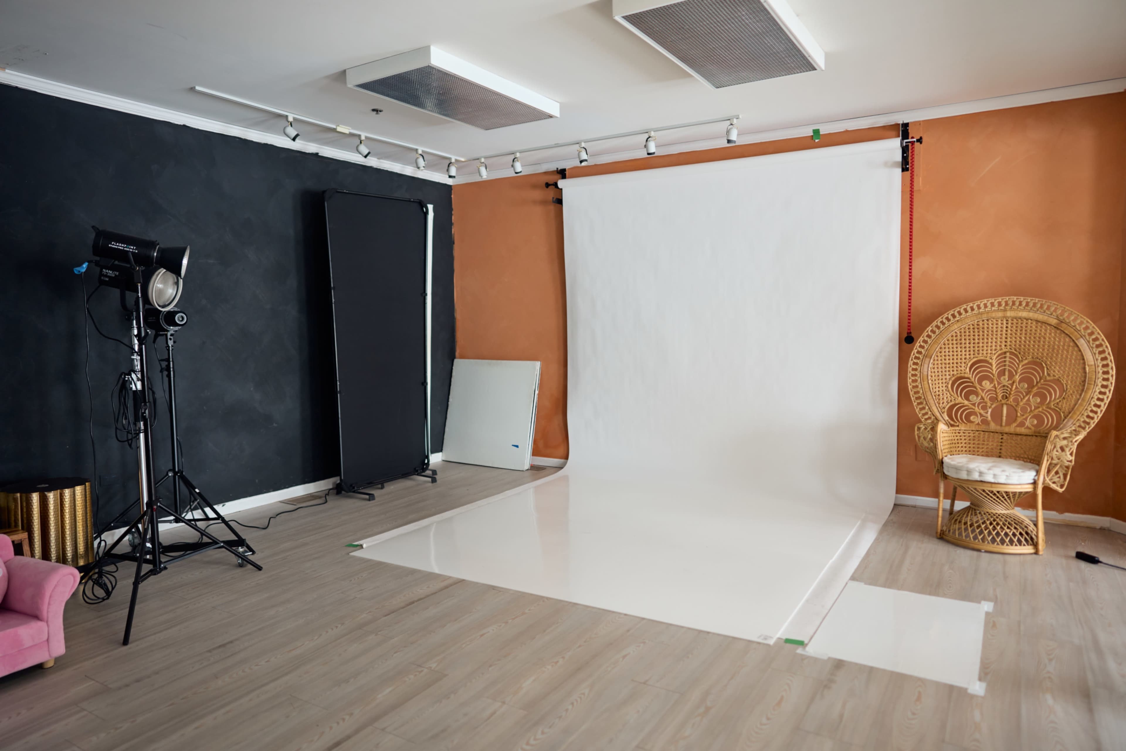 The image shows a photography studio with a large white backdrop, lighting equipment, and a decorative chair against a two-tone wall.