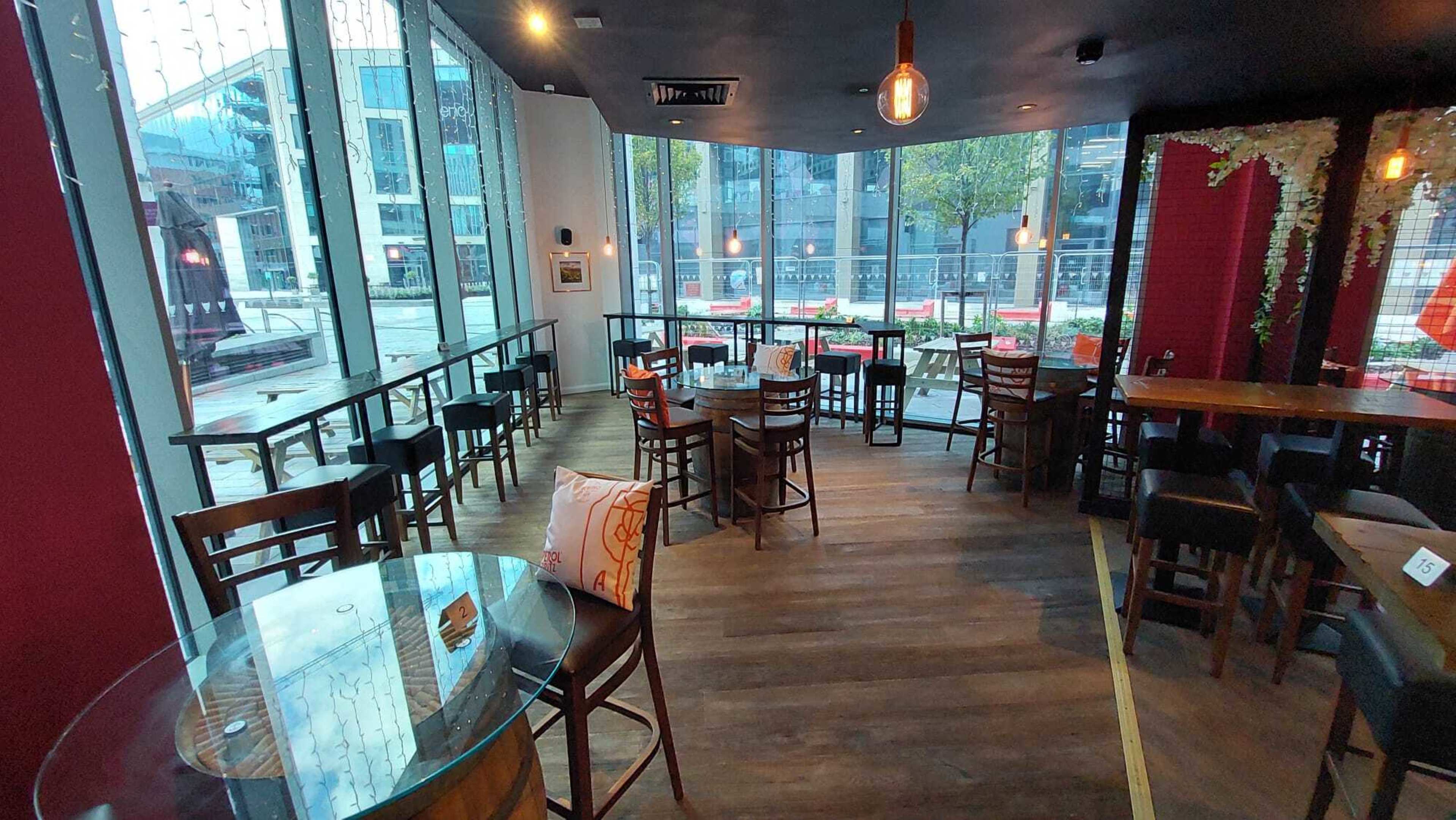 A modern cafe interior with wooden tables and chairs arranged around large windows that face a street.