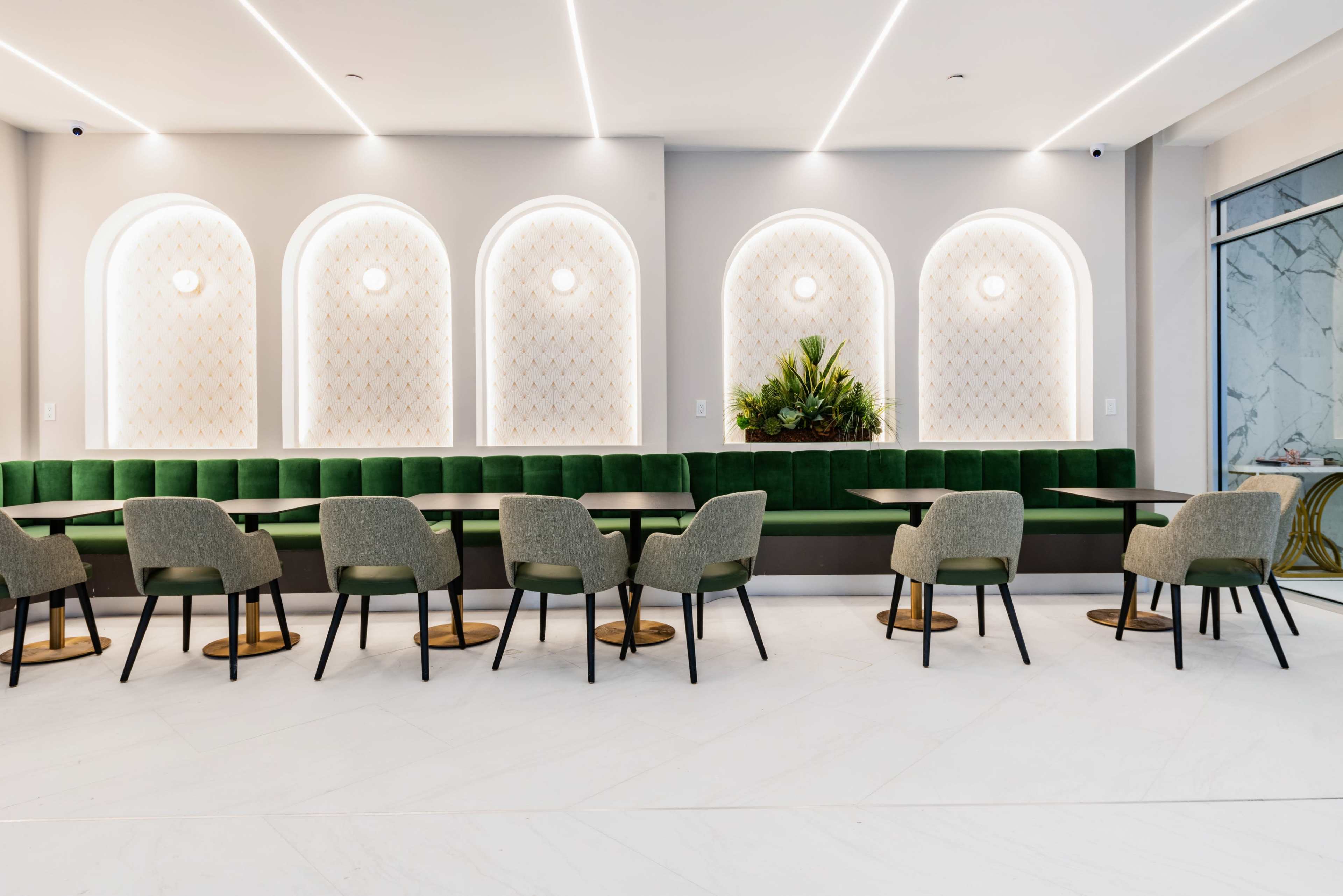The image shows a modern café interior with green upholstered seating, circular light fixtures, and marble accents, arranged with tables and chairs.