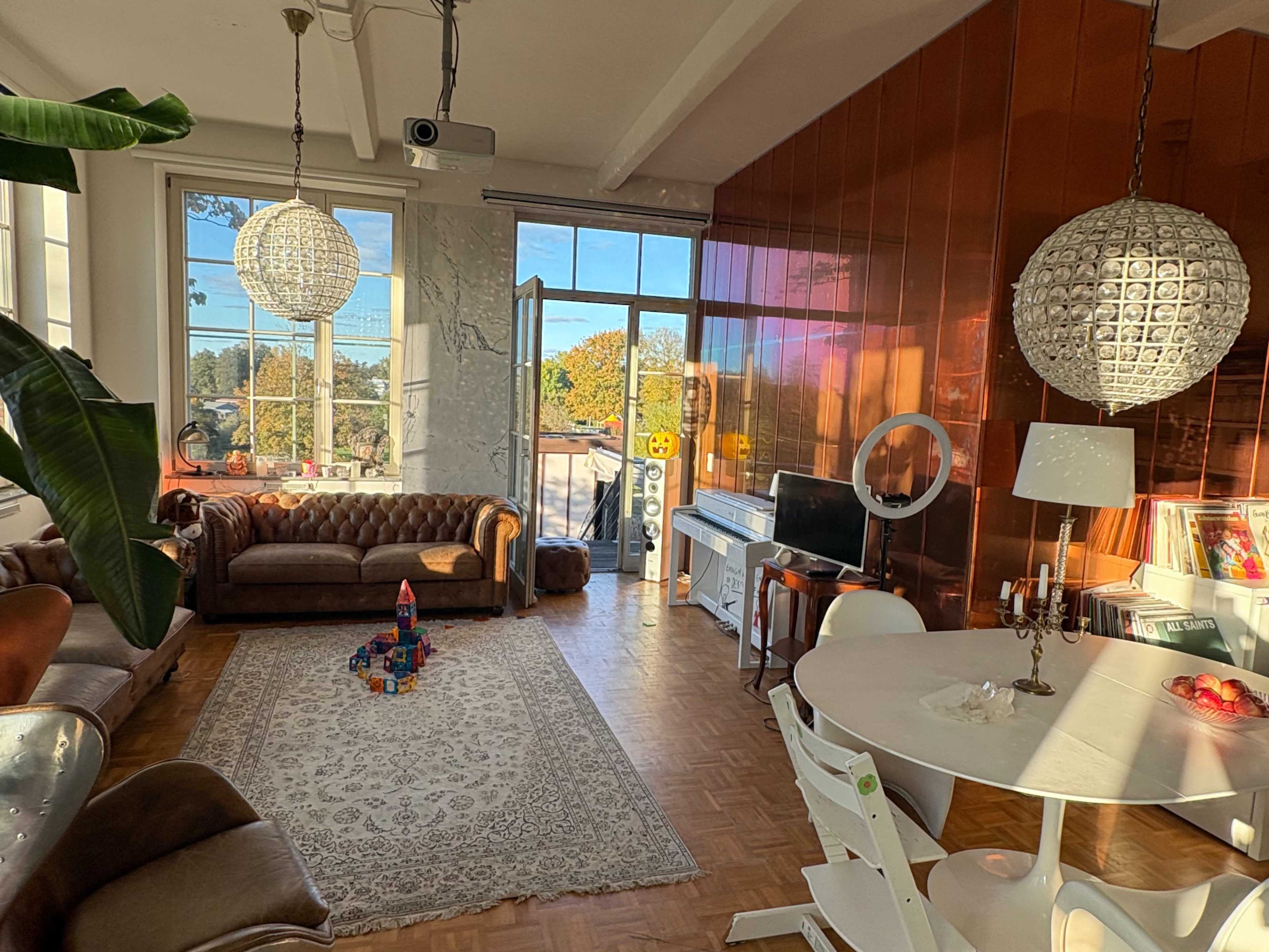 The spacious living area features a mix of brown leather couches, a white dining table, and large windows that let in natural light, showcasing a view outside.