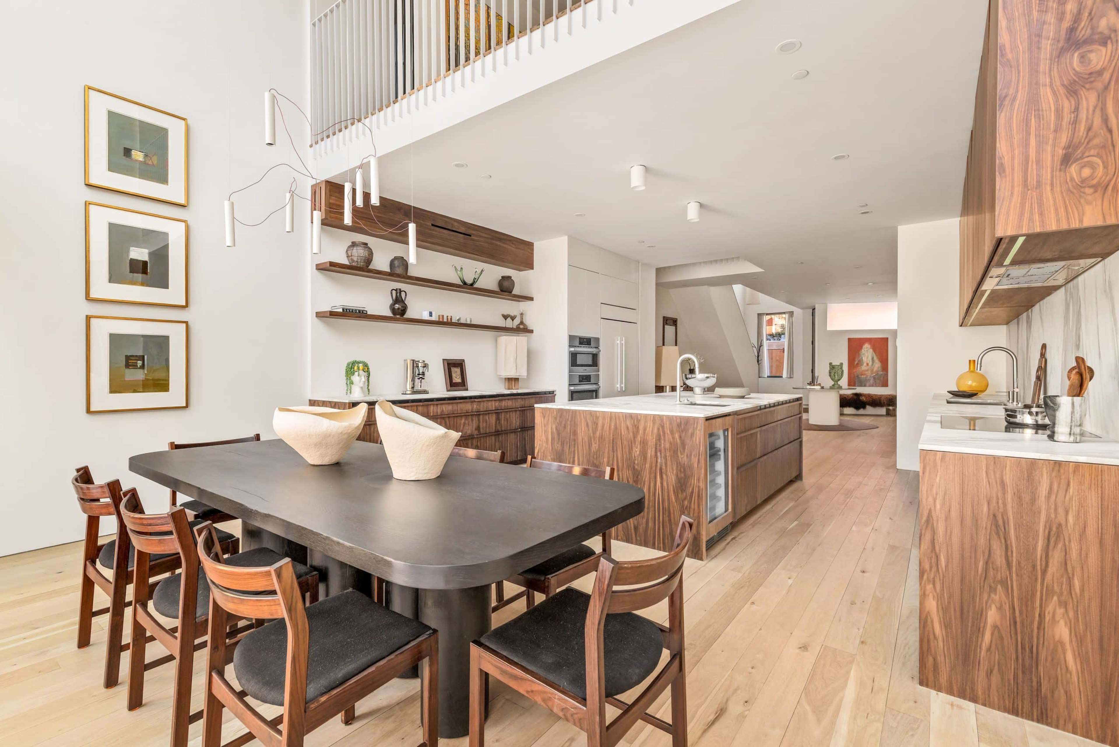A modern kitchen and dining area features wooden cabinetry, a large table with chairs, and an open layout leading to the living space.