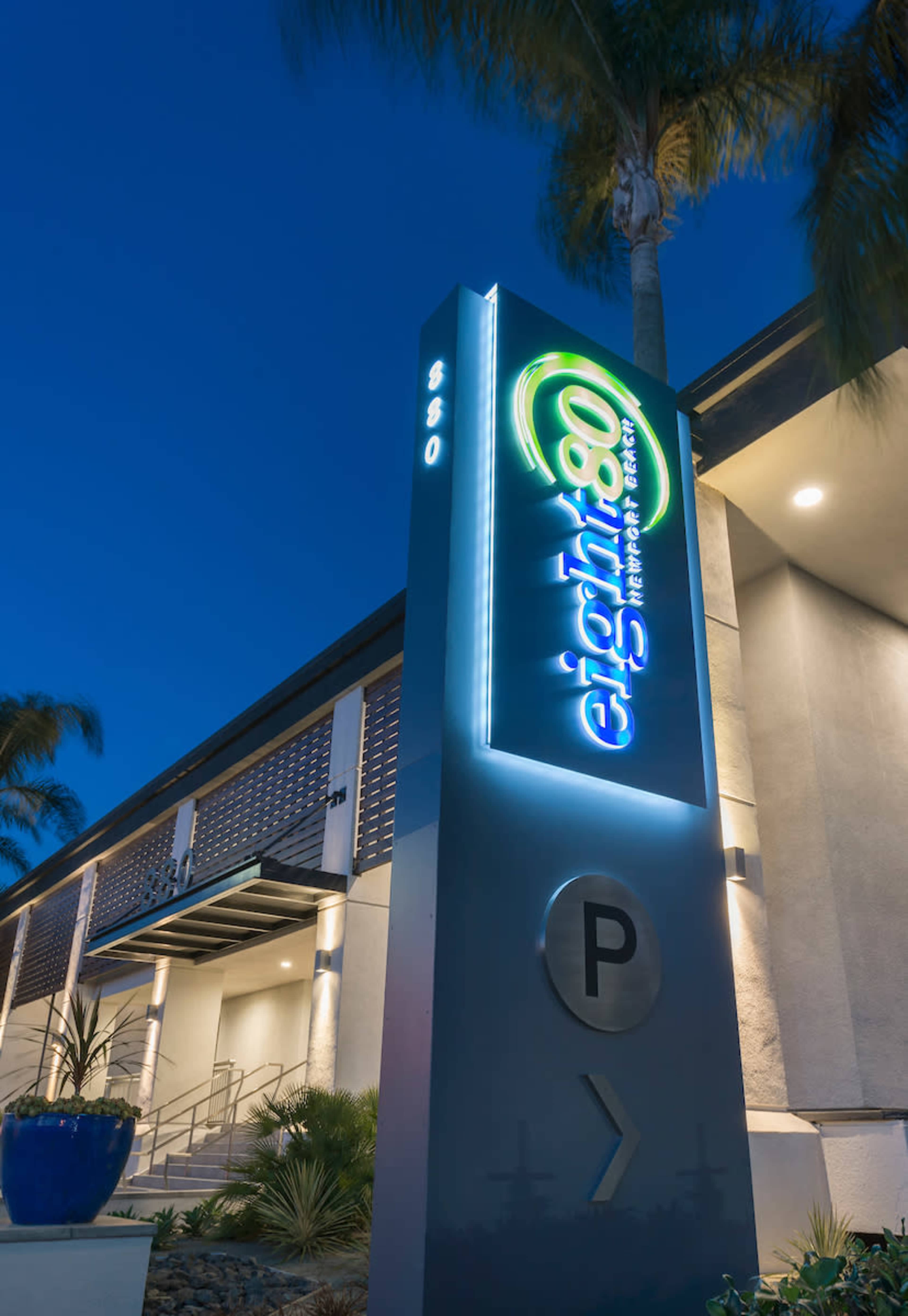 A brightly lit sign for Eight80 Apartments at night, featuring the name and location details along with a parking symbol.