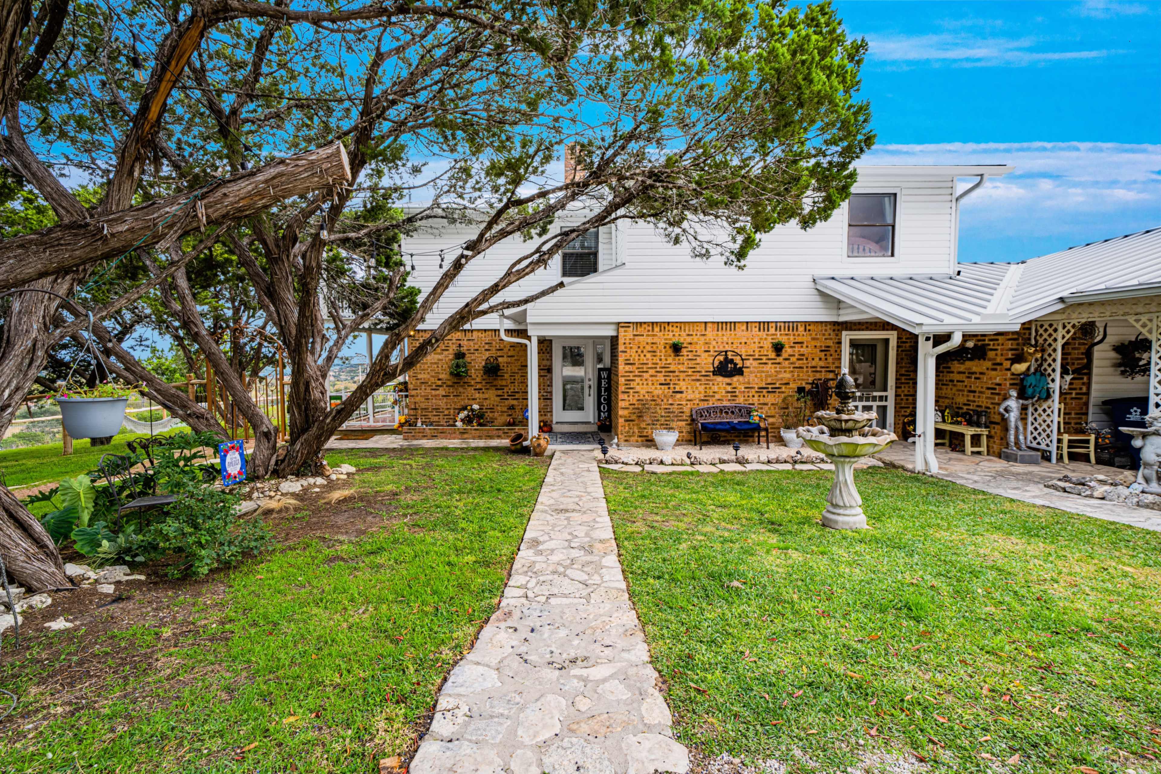 A stone pathway leads to a two-story house surrounded by trees and garden features.