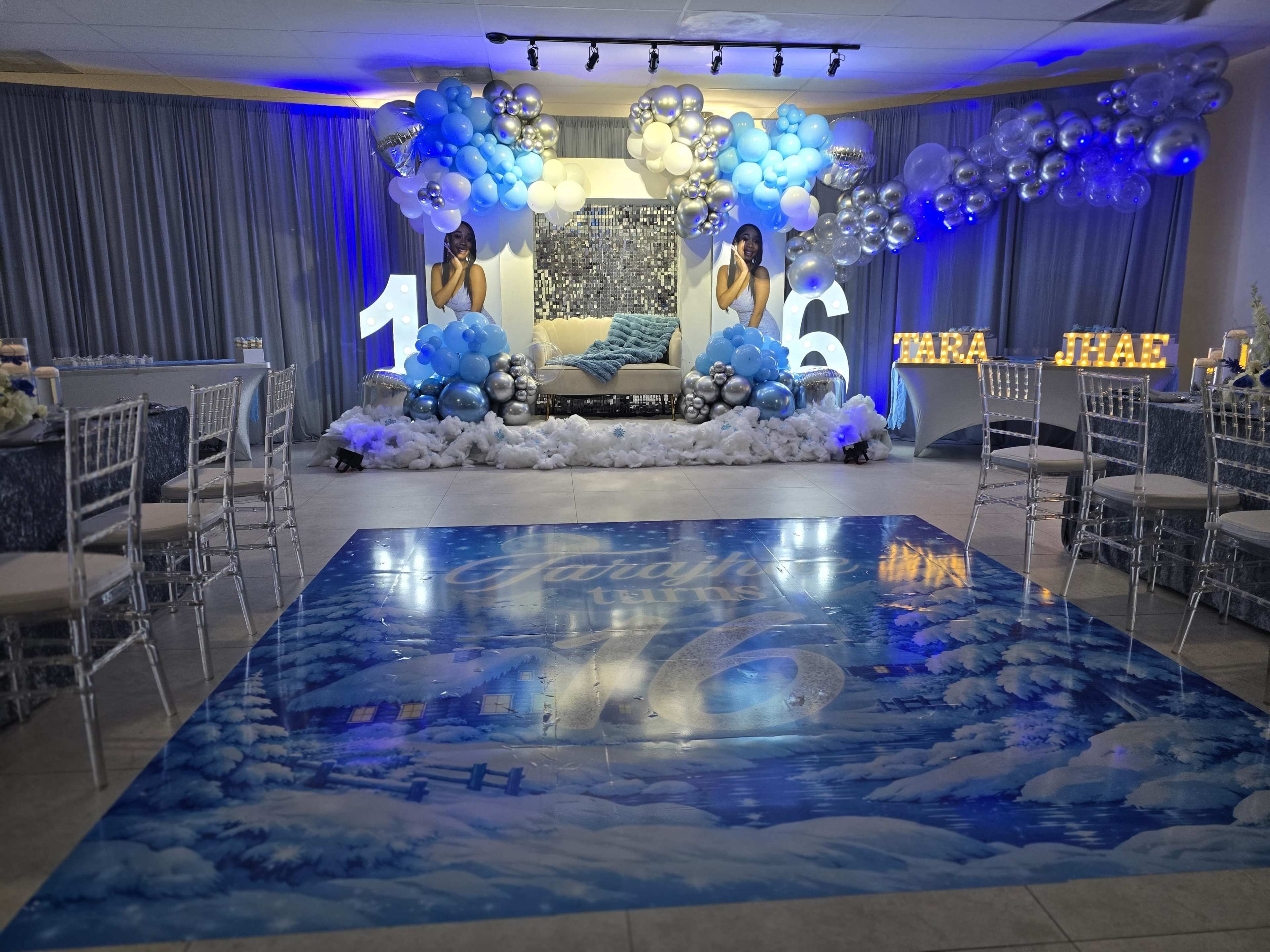 The image shows a decorated event space for a 16th birthday celebration, featuring balloons, large illuminated numbers, and a winter-themed backdrop.