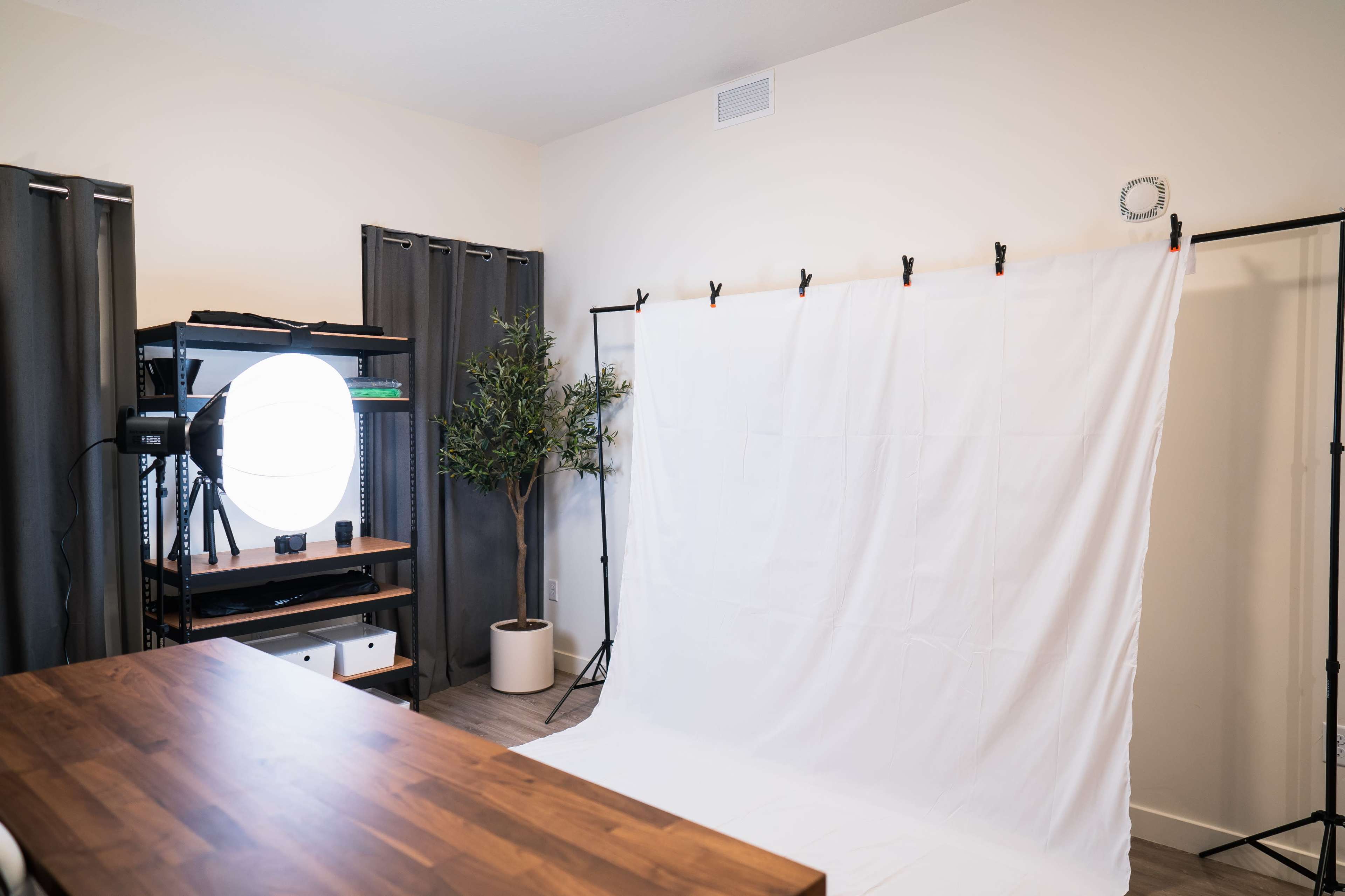 A photography studio setup with a white backdrop, a lighting setup, and a wooden table in a well-lit room.