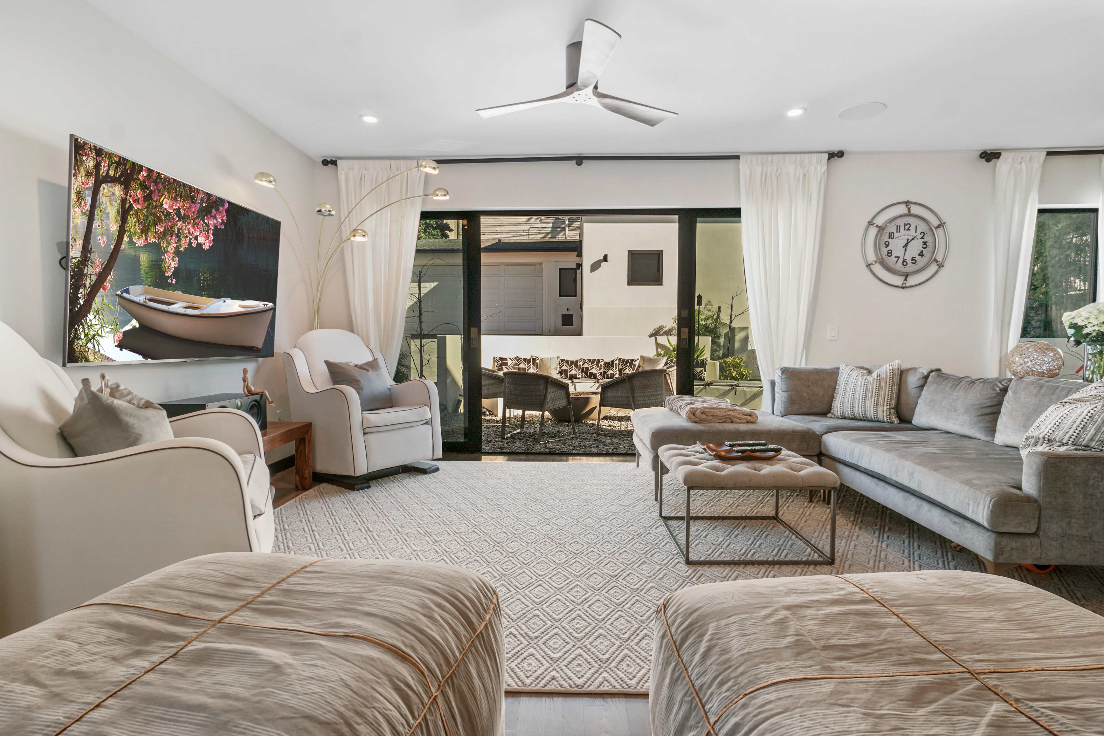 A contemporary living room with modern furniture, a large TV on the wall, and glass doors leading to an outdoor area.