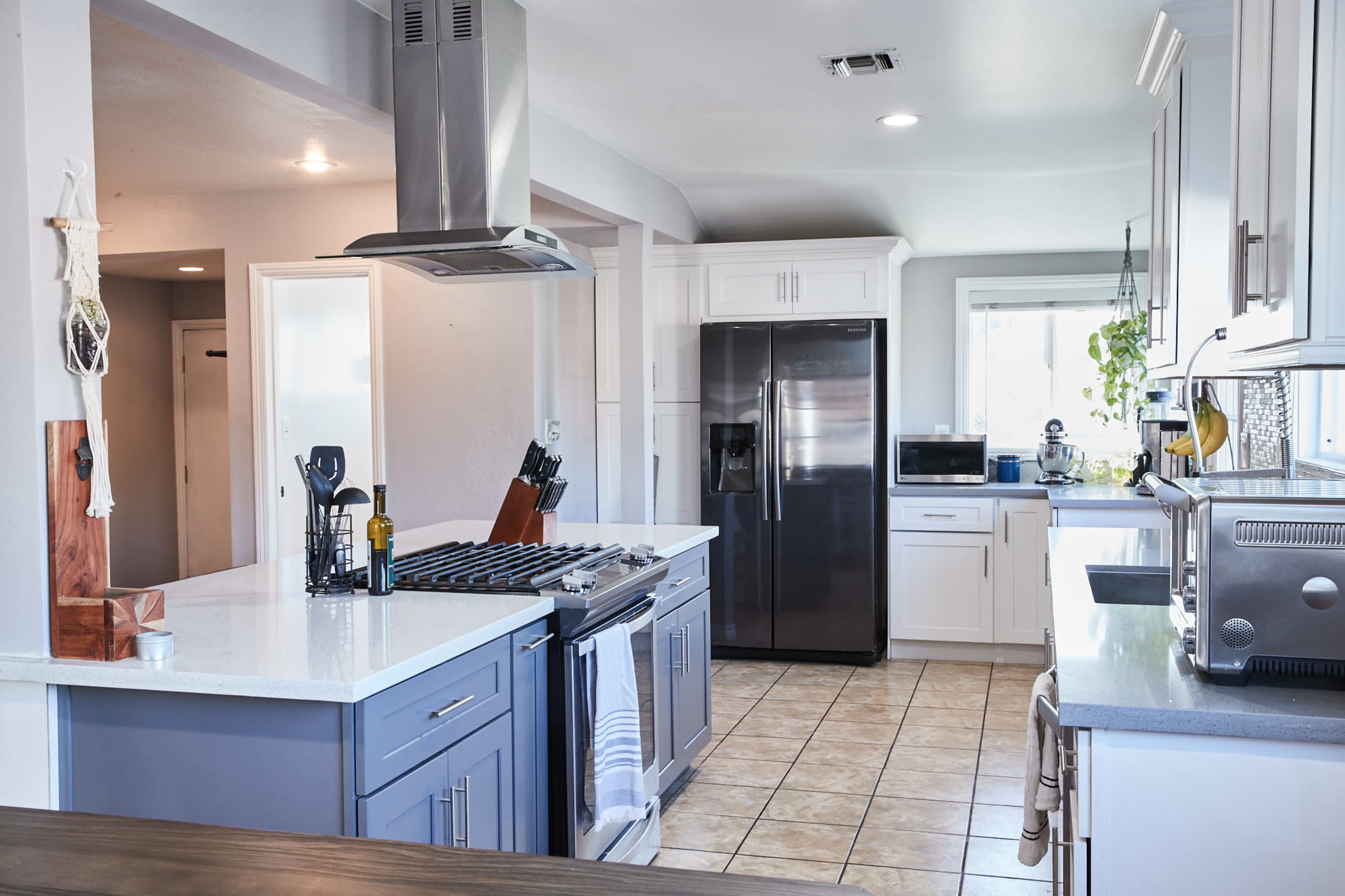 A modern kitchen features a large island with a gas stove, stainless steel appliances, and a window with natural light.