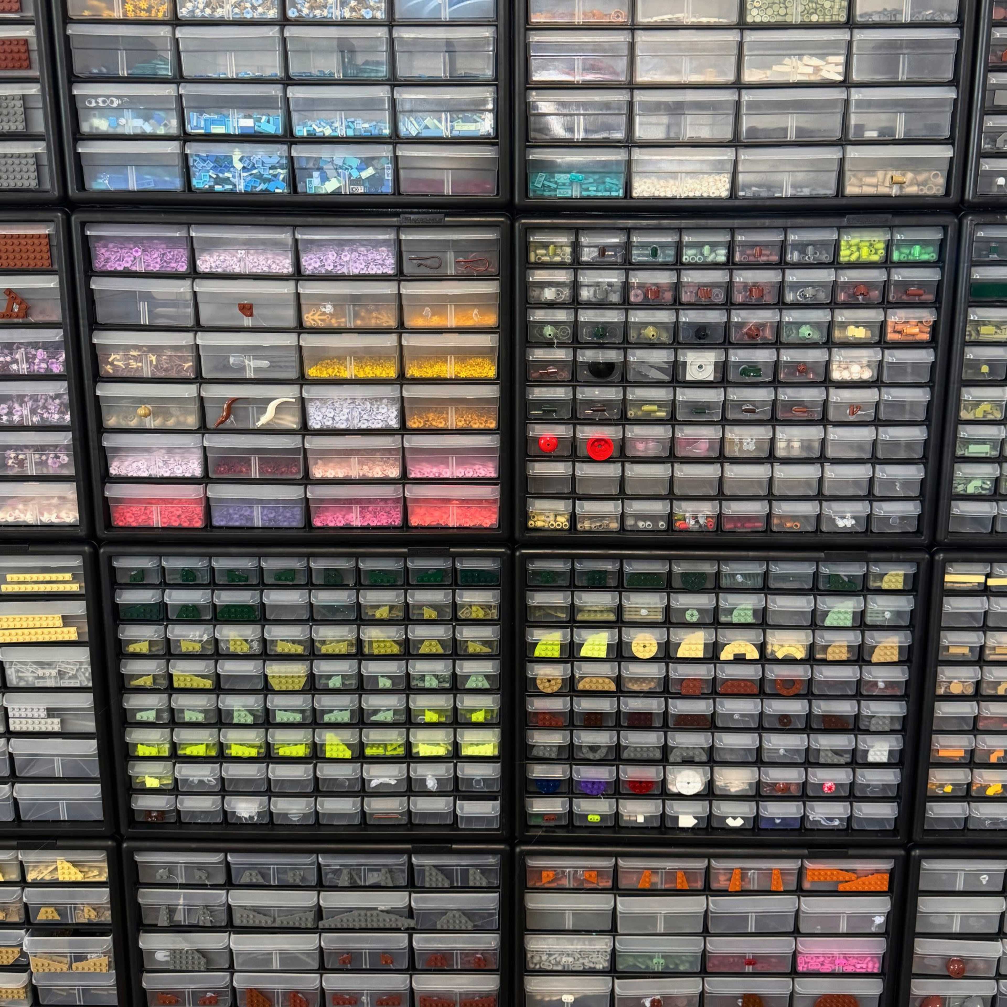 The image shows a wall-mounted storage unit filled with numerous transparent bins containing various small, colorful items organized by type.