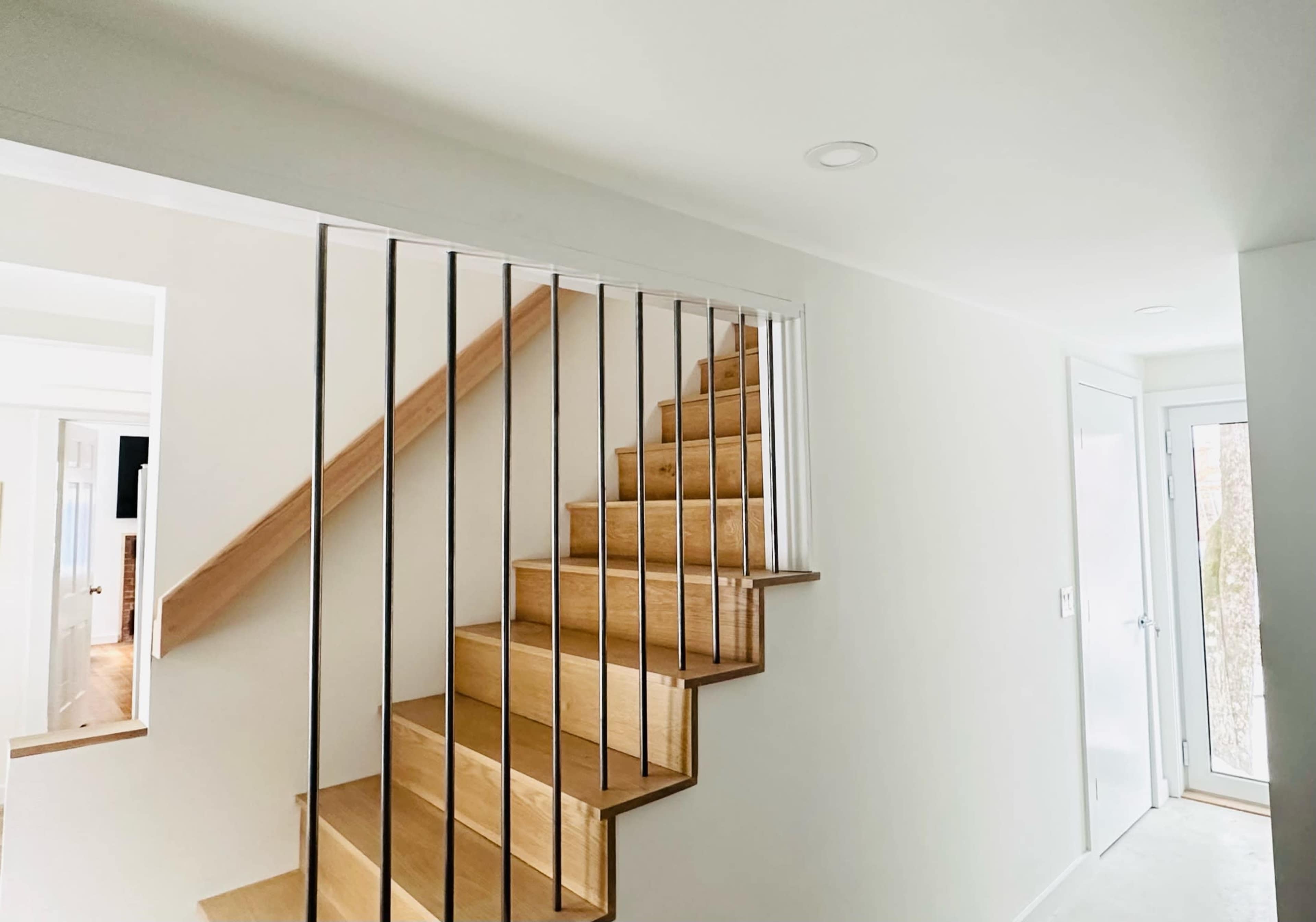 A wooden staircase with a sleek railing leads up to a light-colored upper level in a modern interior space.