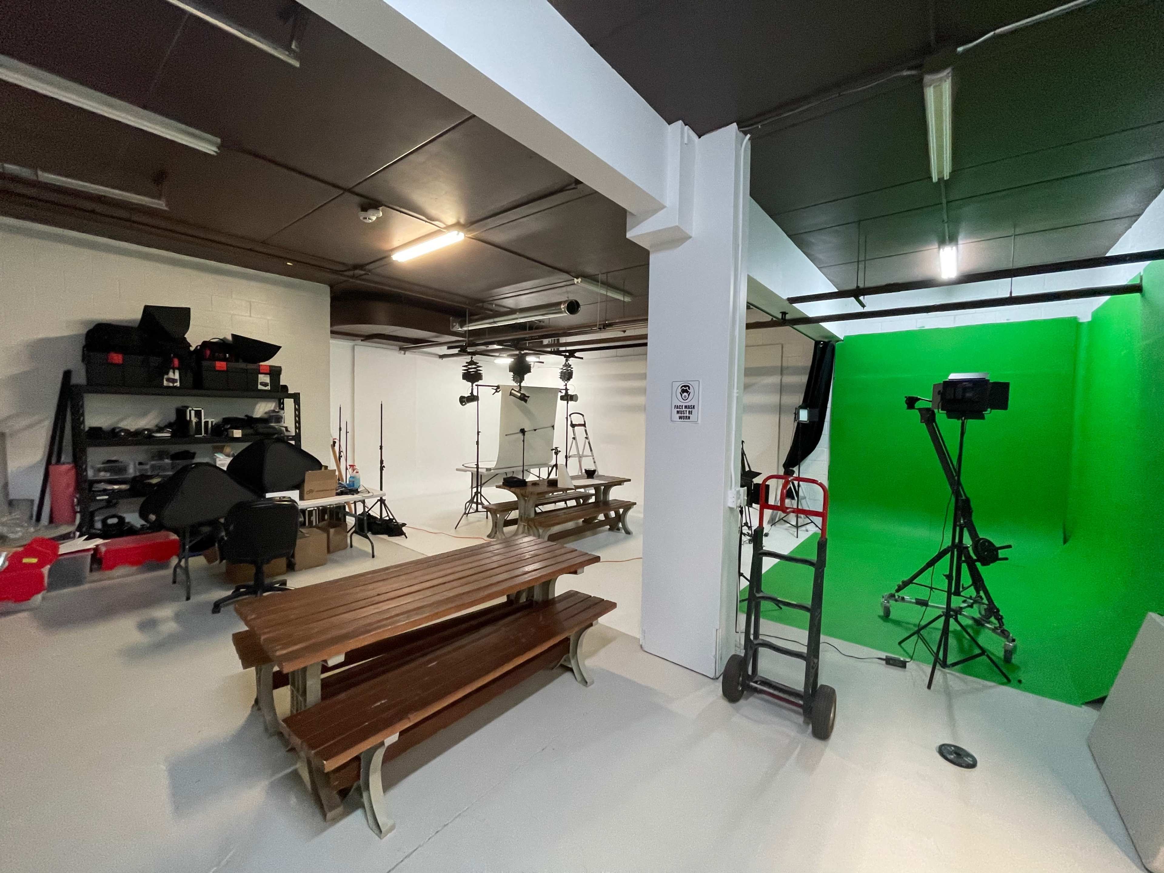 A spacious studio with a green screen setup, tables, lighting equipment, and various photography props neatly arranged on shelves.