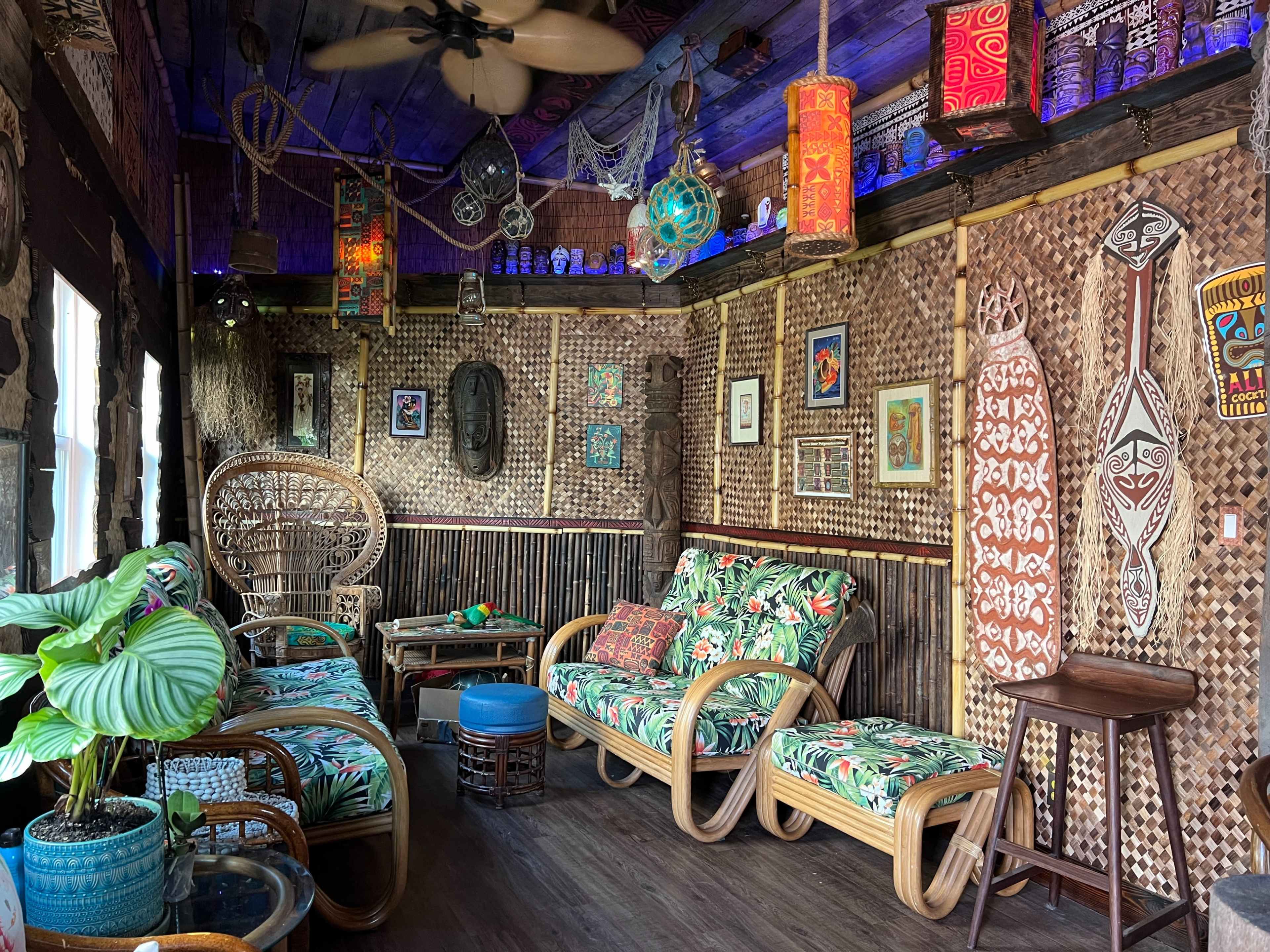A tropical-themed room with woven walls, patterned furniture, and decorative artifacts arranged around a seating area.