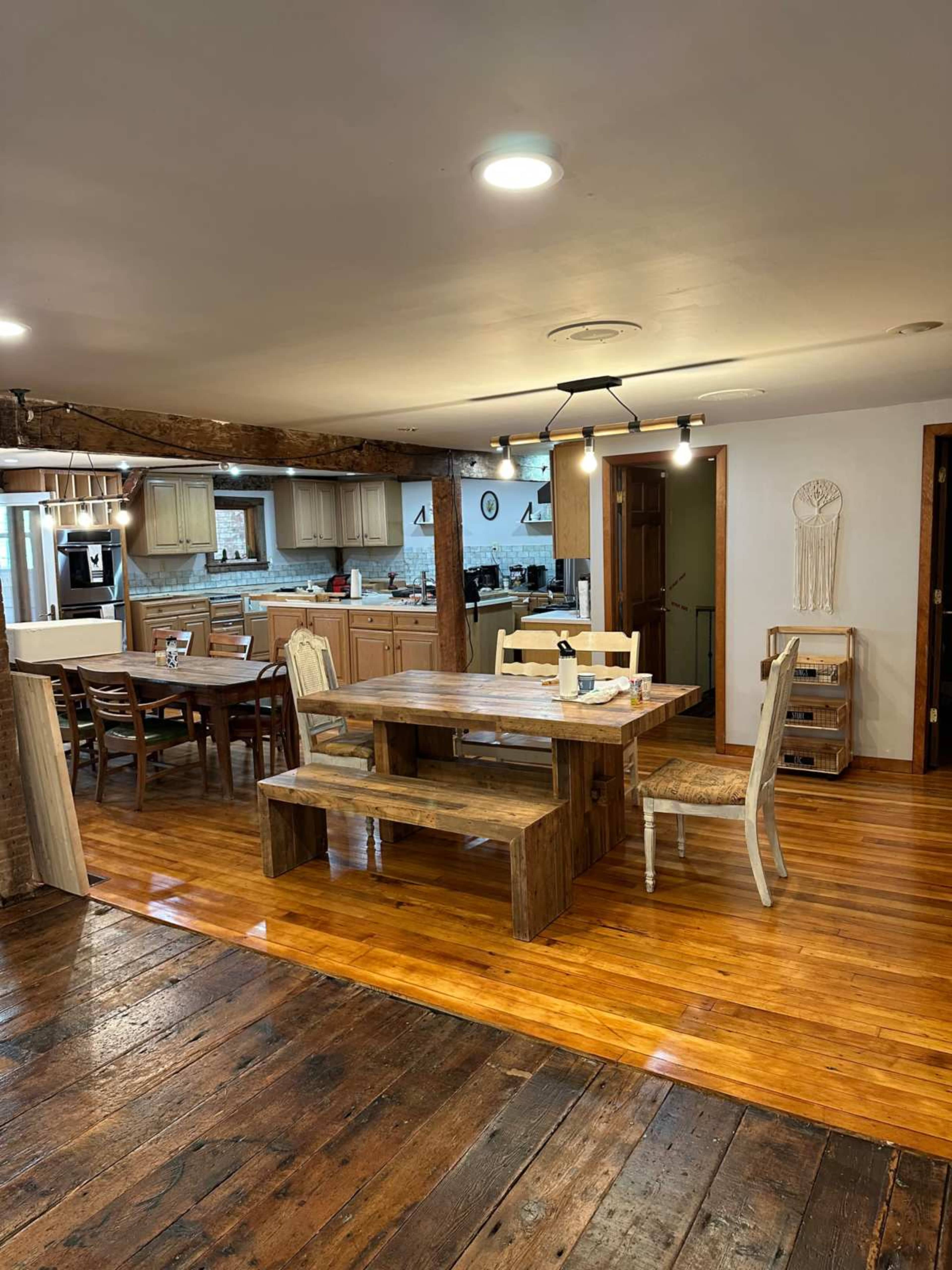 The image shows a spacious dining area with a wooden table and chairs, connected to a kitchen in a rustic-style interior.