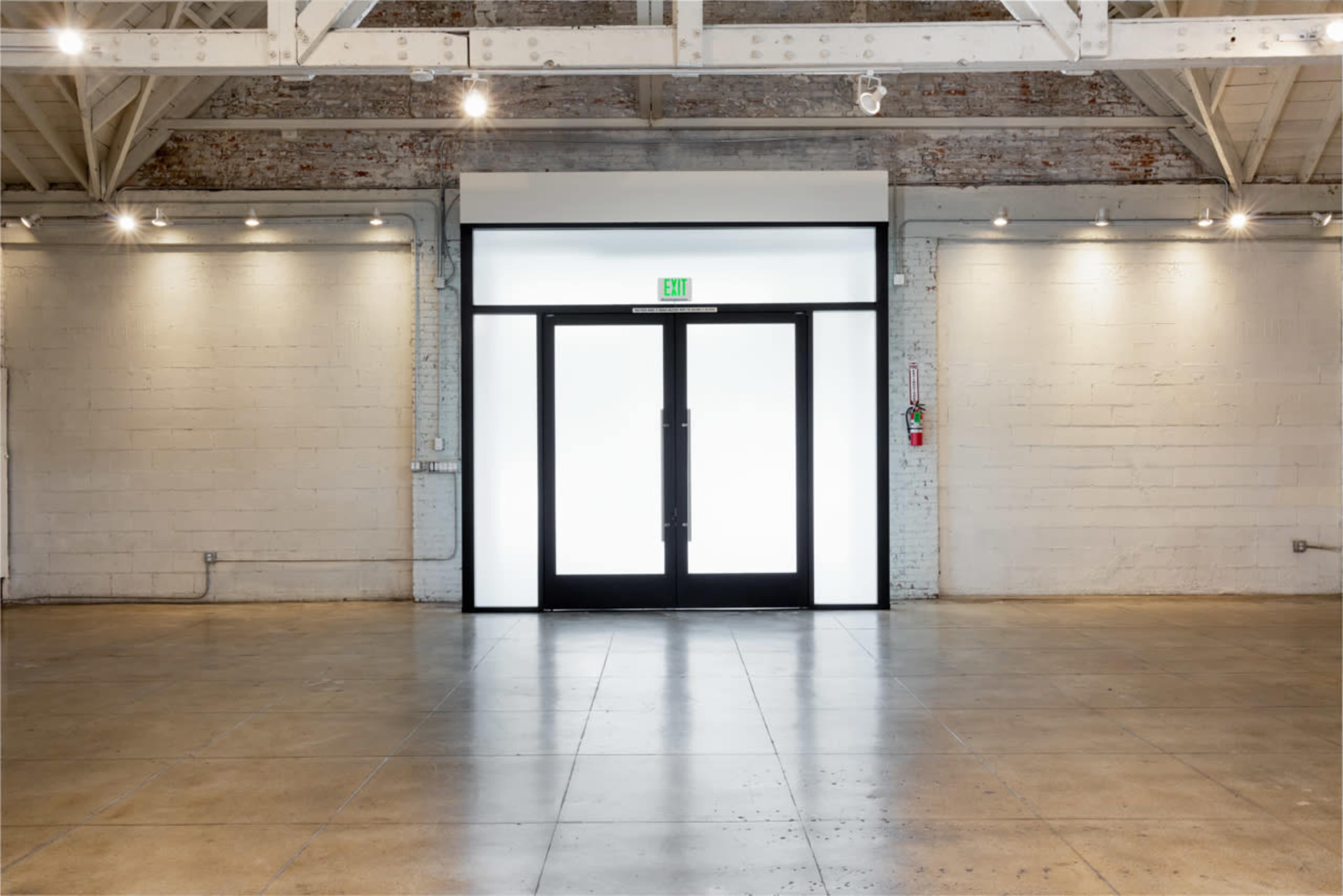 The image shows an empty room with a large double door at the center, illuminated by bright light from outside.