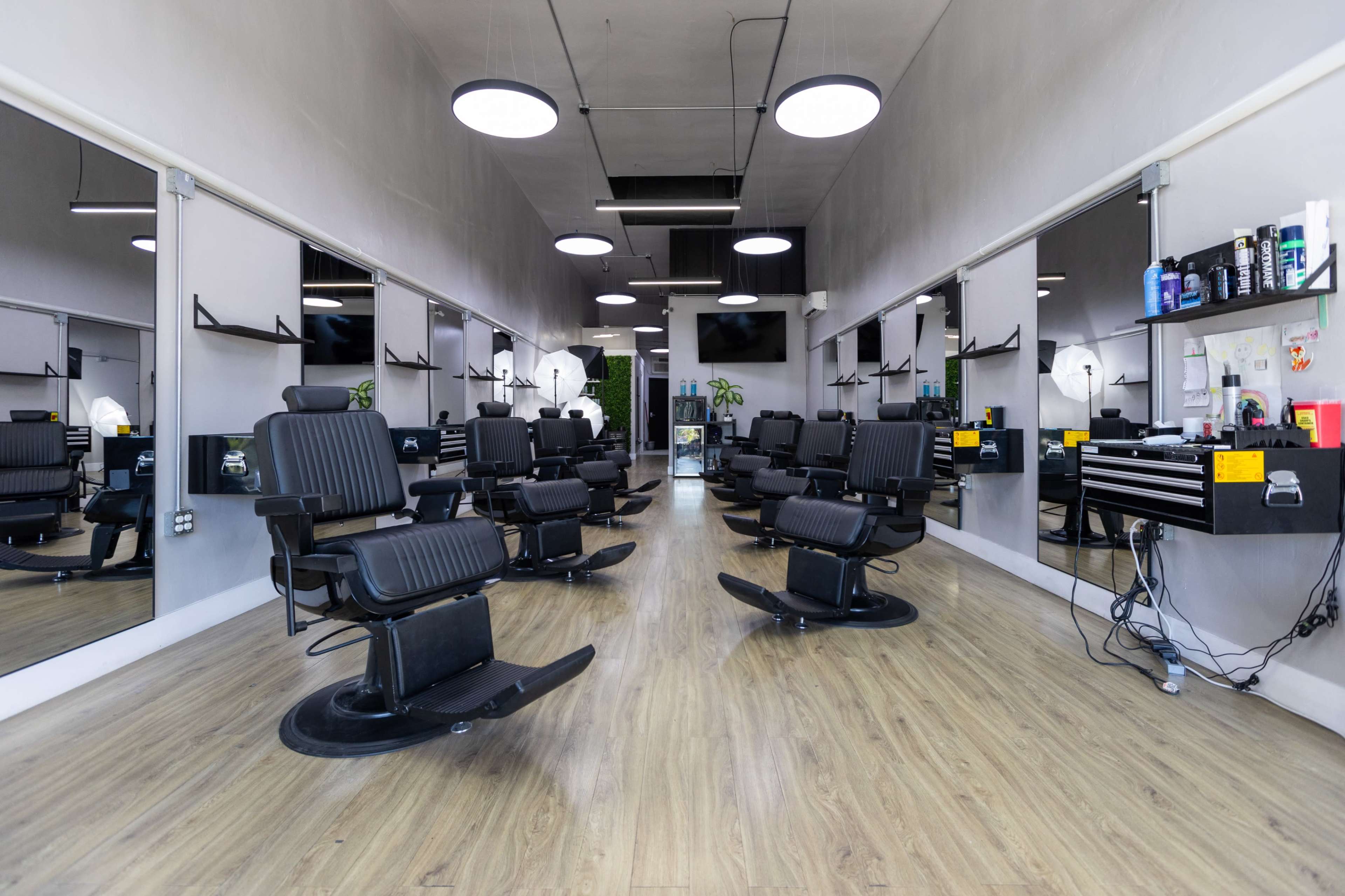 The image shows an interior of a modern barbershop with multiple styling chairs, large mirrors, and a clean, minimalist design.