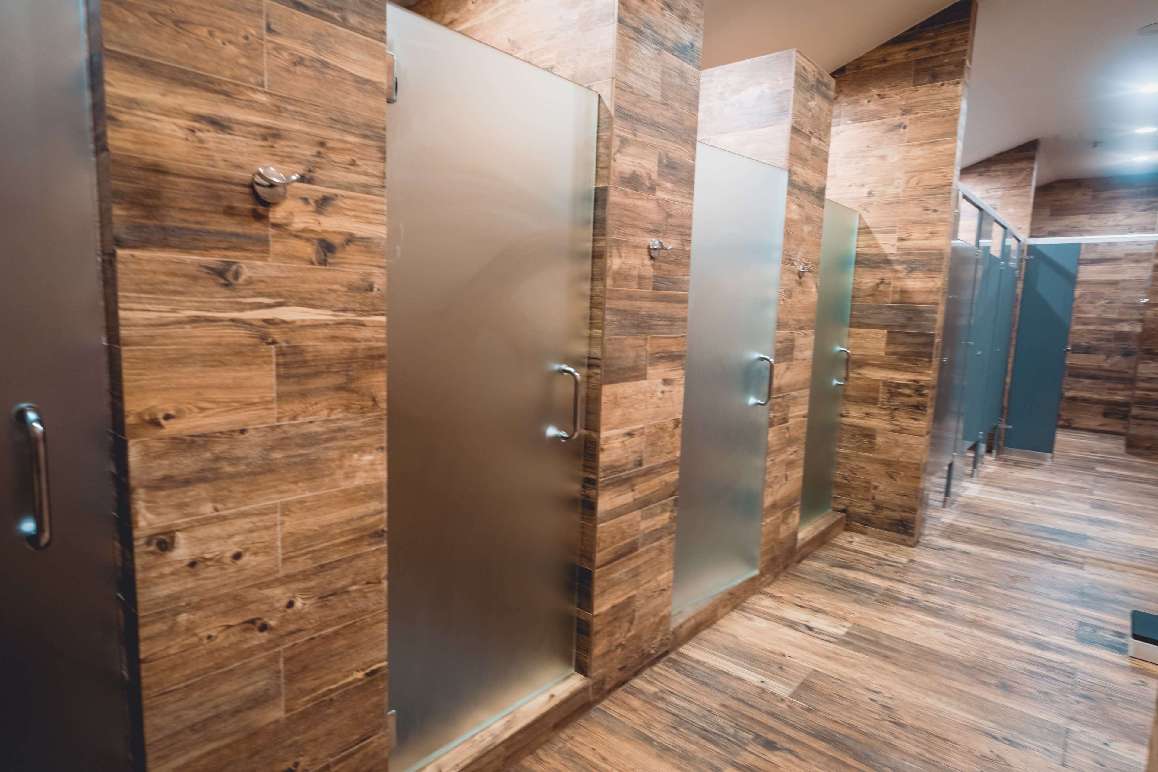 A row of shower stalls with frosted glass doors, surrounded by wooden paneling and a wooden floor.