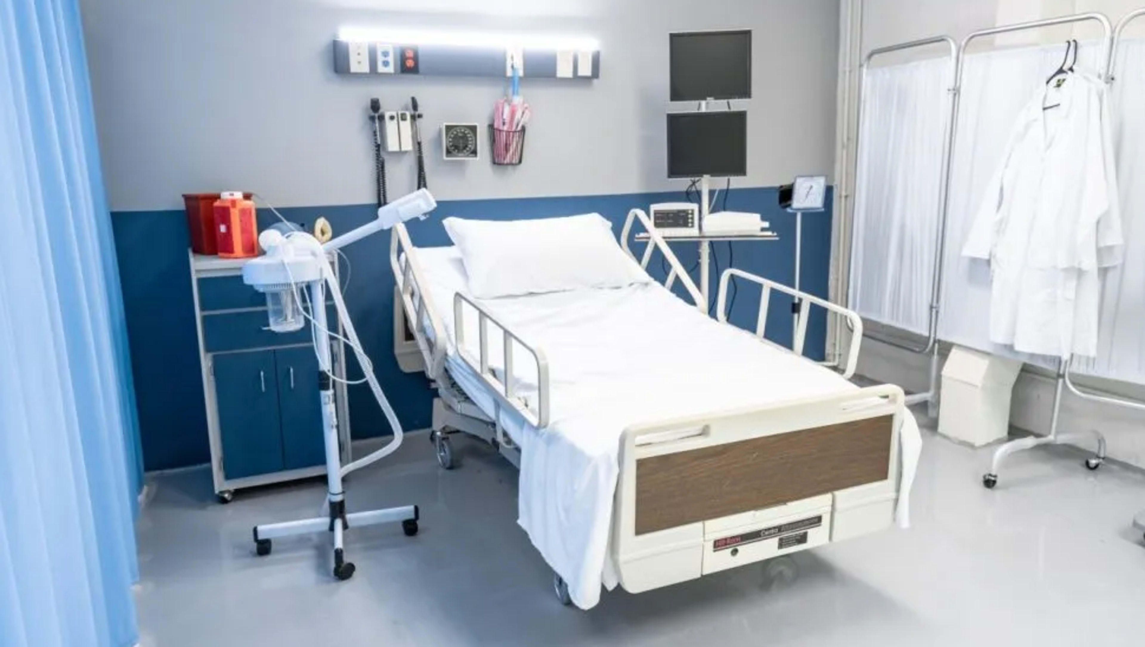 The image shows a hospital room featuring a bed, medical equipment, and a cabinet against a blue and gray wall.