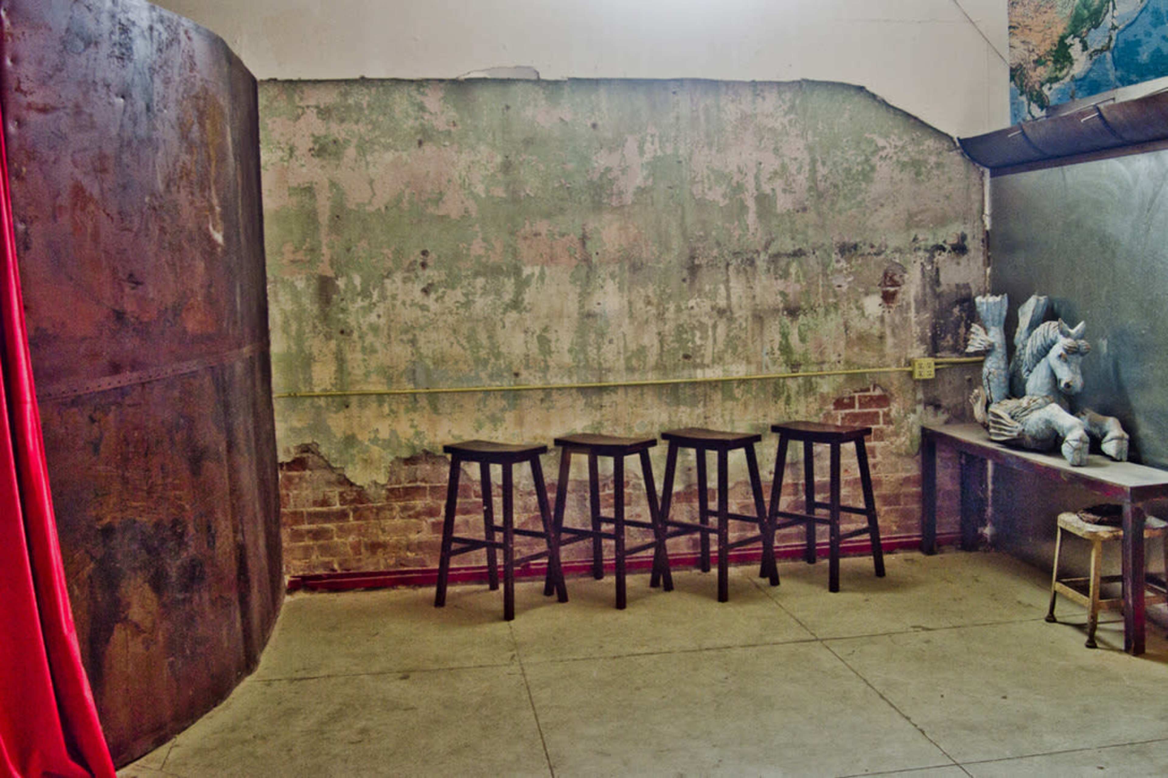 A sparse interior space with a textured wall, four black stools in a row, and a table with a sculpted figure on it.