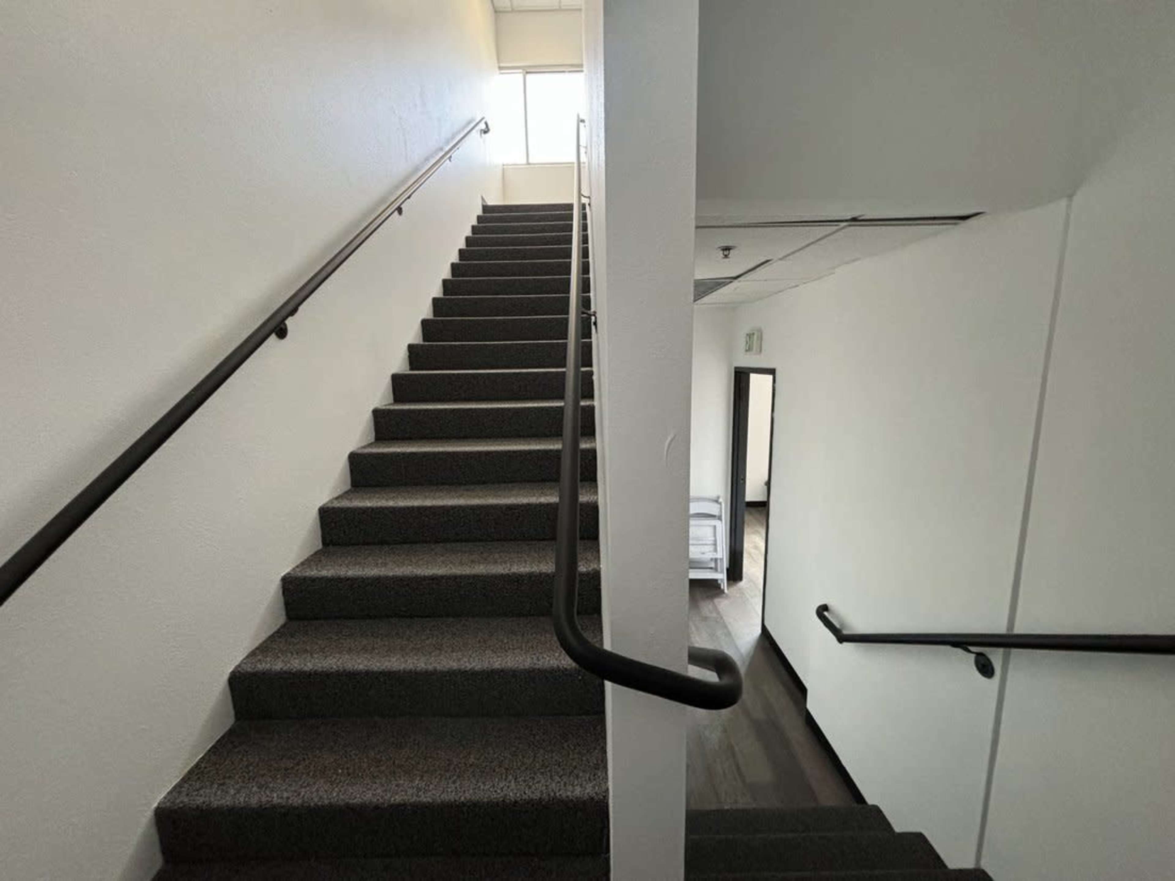 A stairwell with light-colored walls and carpeted stairs leading up to a landing with a window.